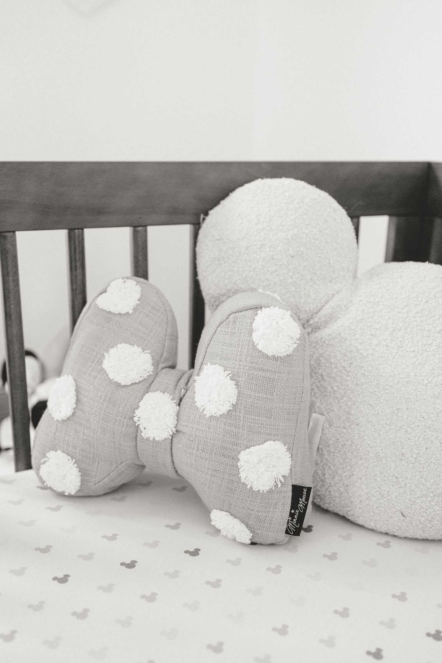 Gray and white polka dot stuffed elephant toy in wooden crib with Mickey Mouse bedding.