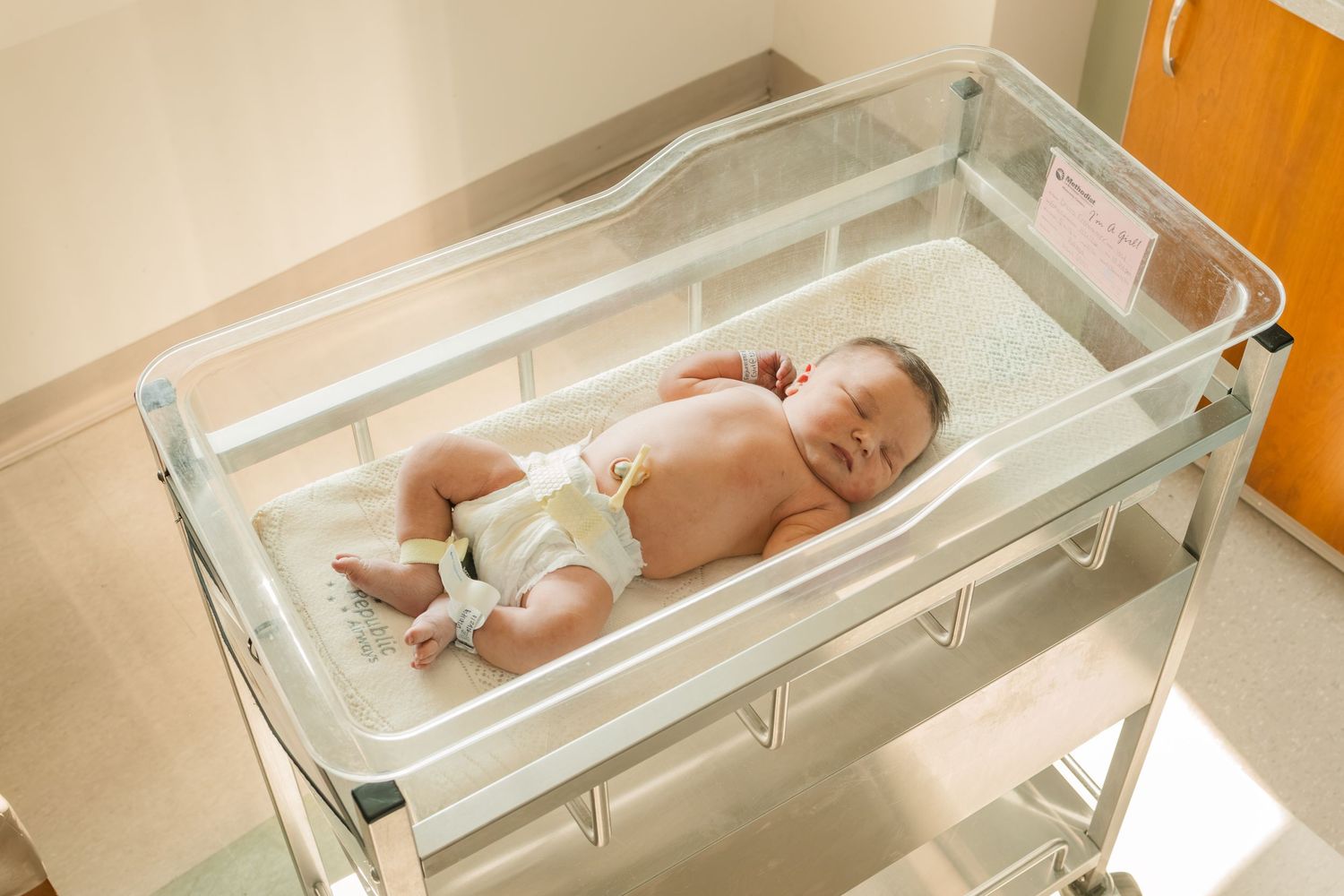 Newborn baby sleeping peacefully in a hospital bassinet wearing a diaper.