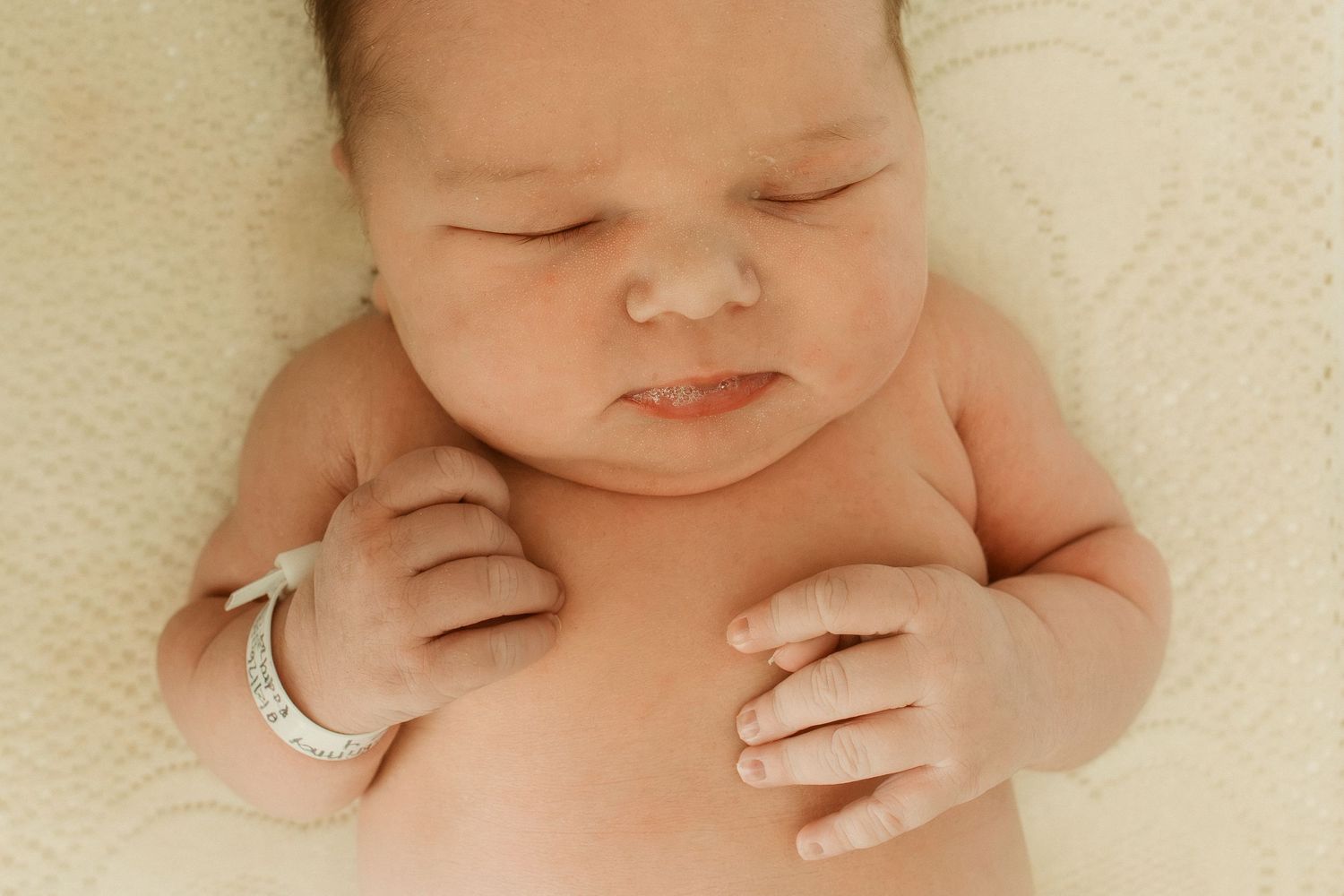 Peaceful newborn baby sleeping on white blanket wearing hospital ID bracelet.