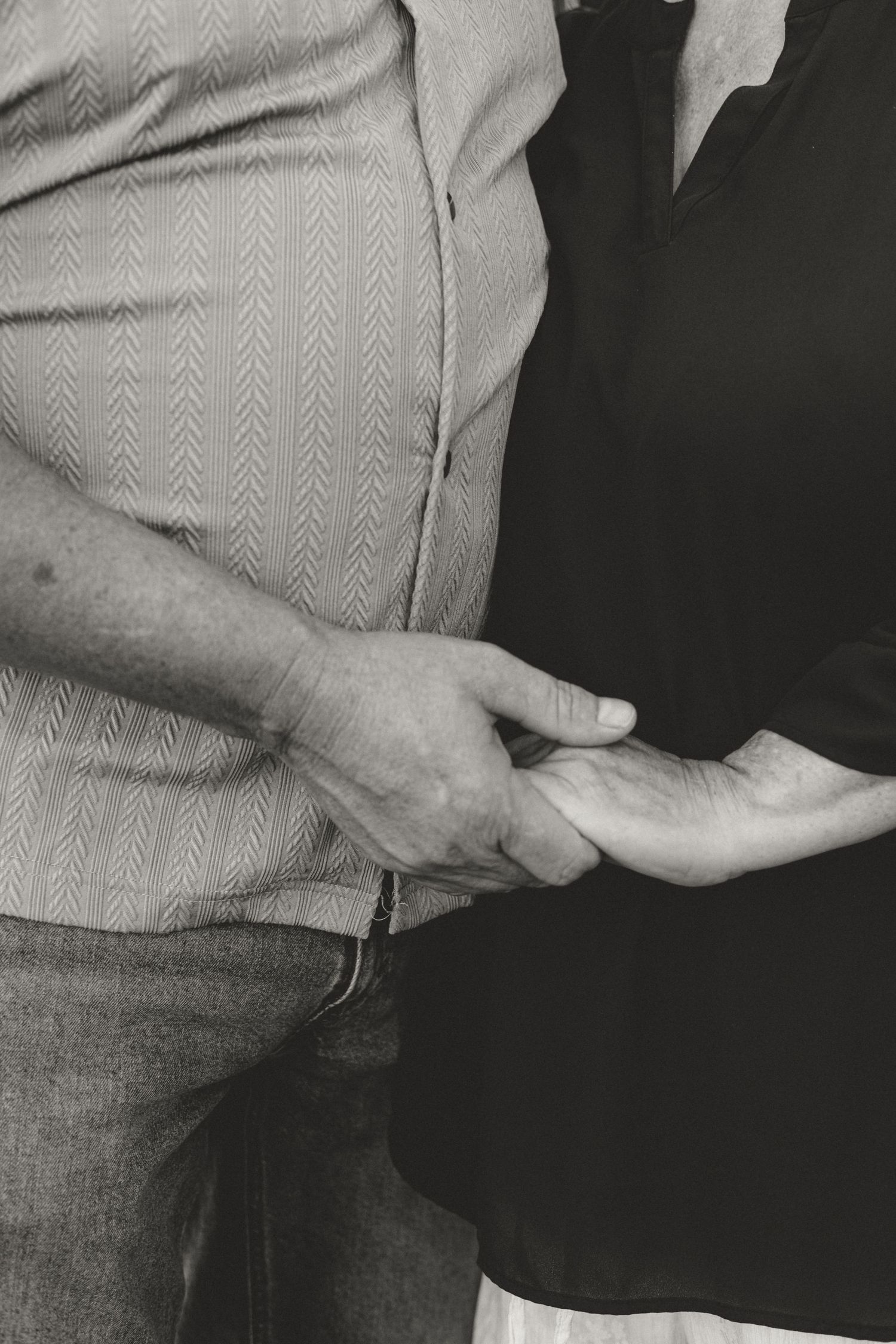 Close-up black and white photo of a couple gently holding hands, showing tender connection and togetherness.