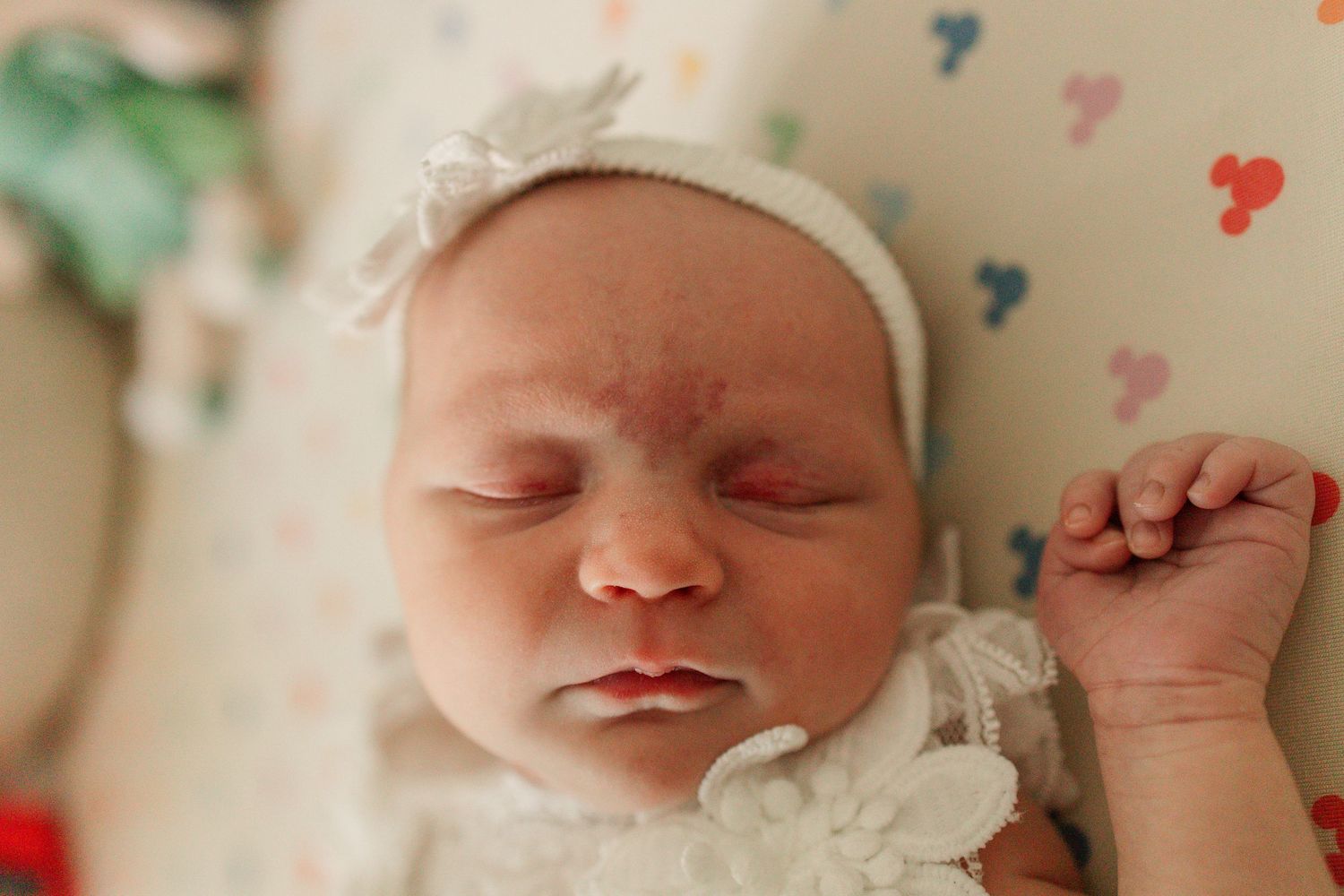 Close-up portrait of a sleeping newborn baby wearing a white floral headband.