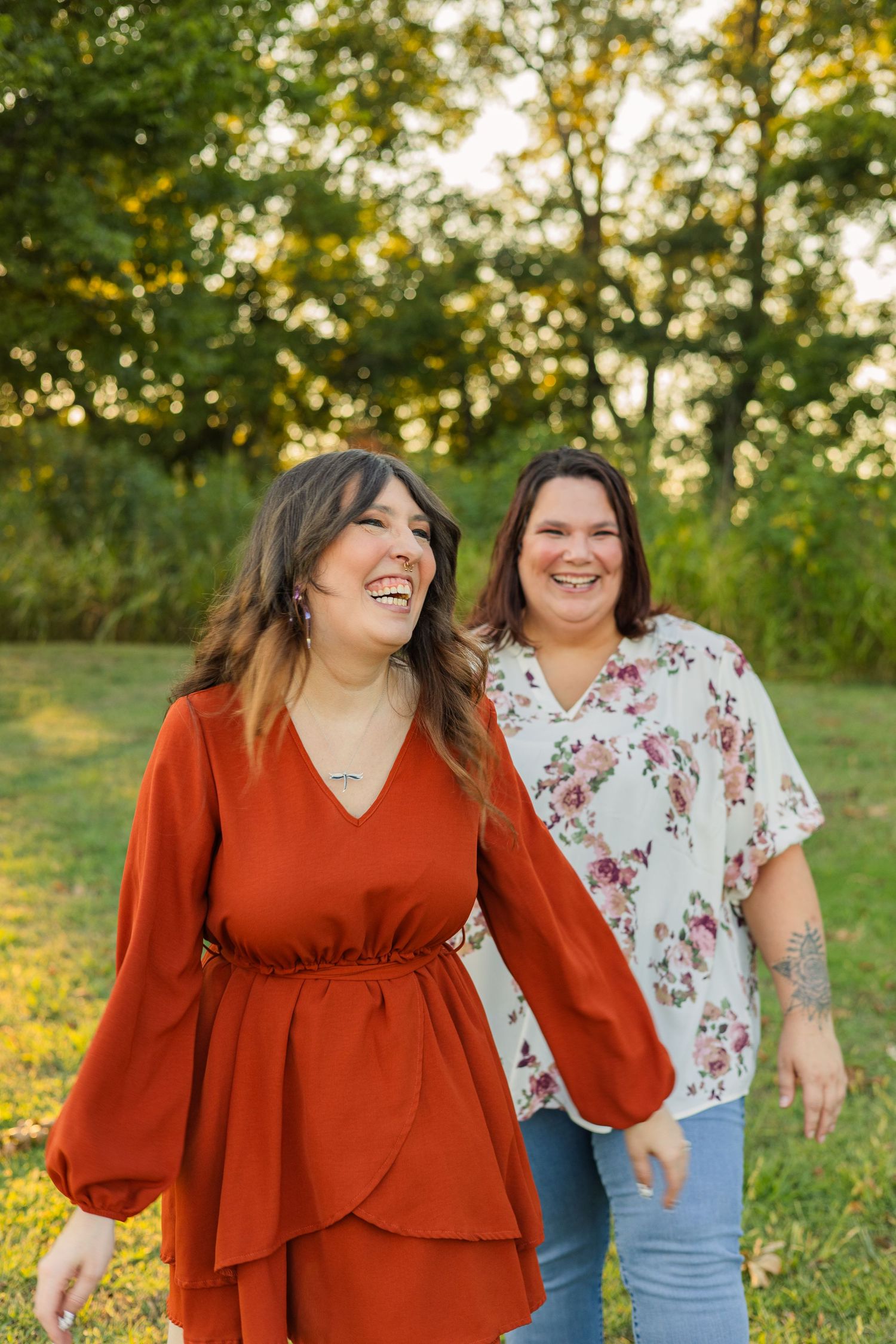 Two women laughing and walking together outdoors in a sunny green park setting.