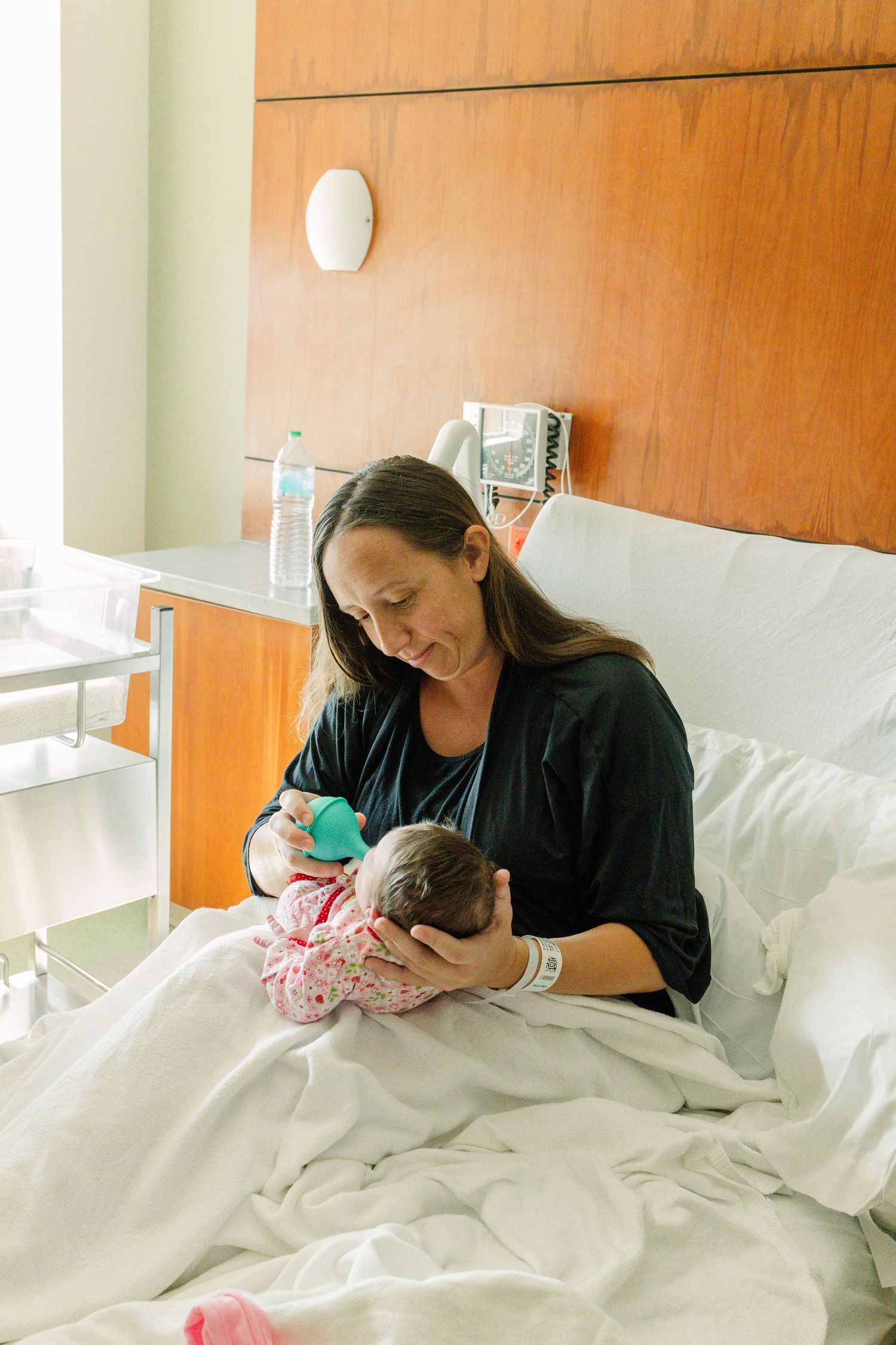New mother breastfeeding newborn baby while sitting in hospital bed.