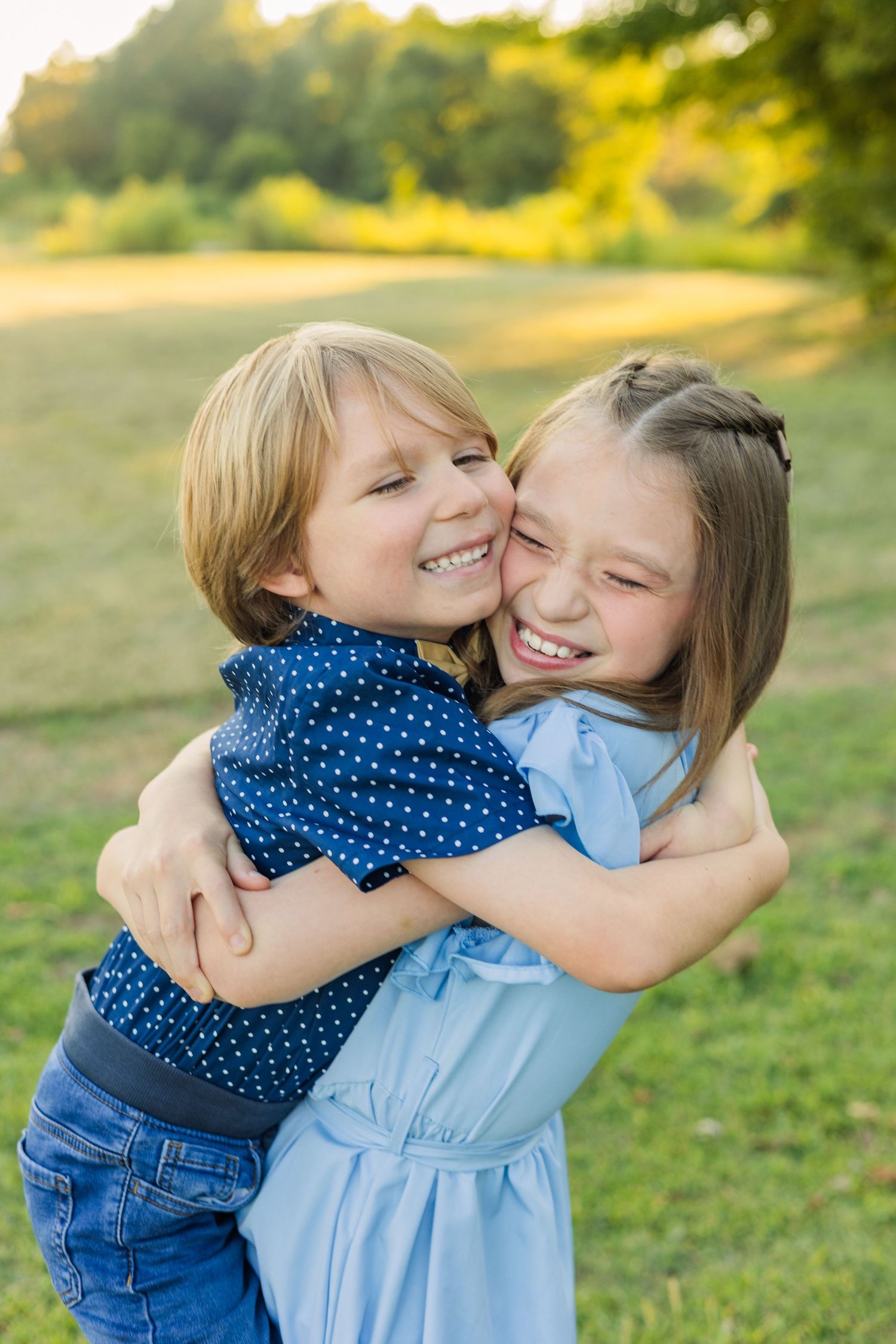 Two happy children hugging and laughing together outdoors in a sunny green park setting.