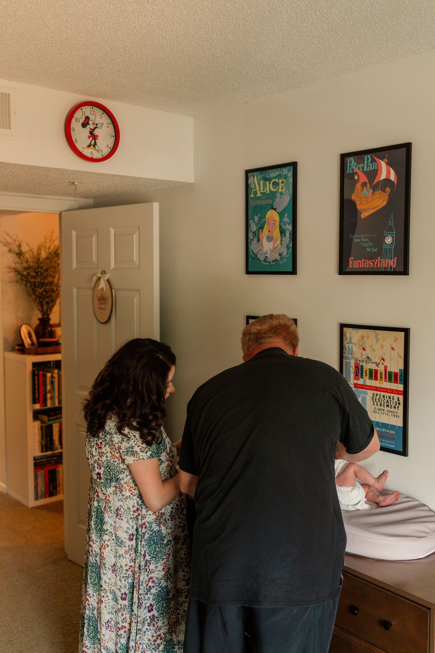 Couple standing at changing table in Disney-themed nursery with vintage movie posters on wall.