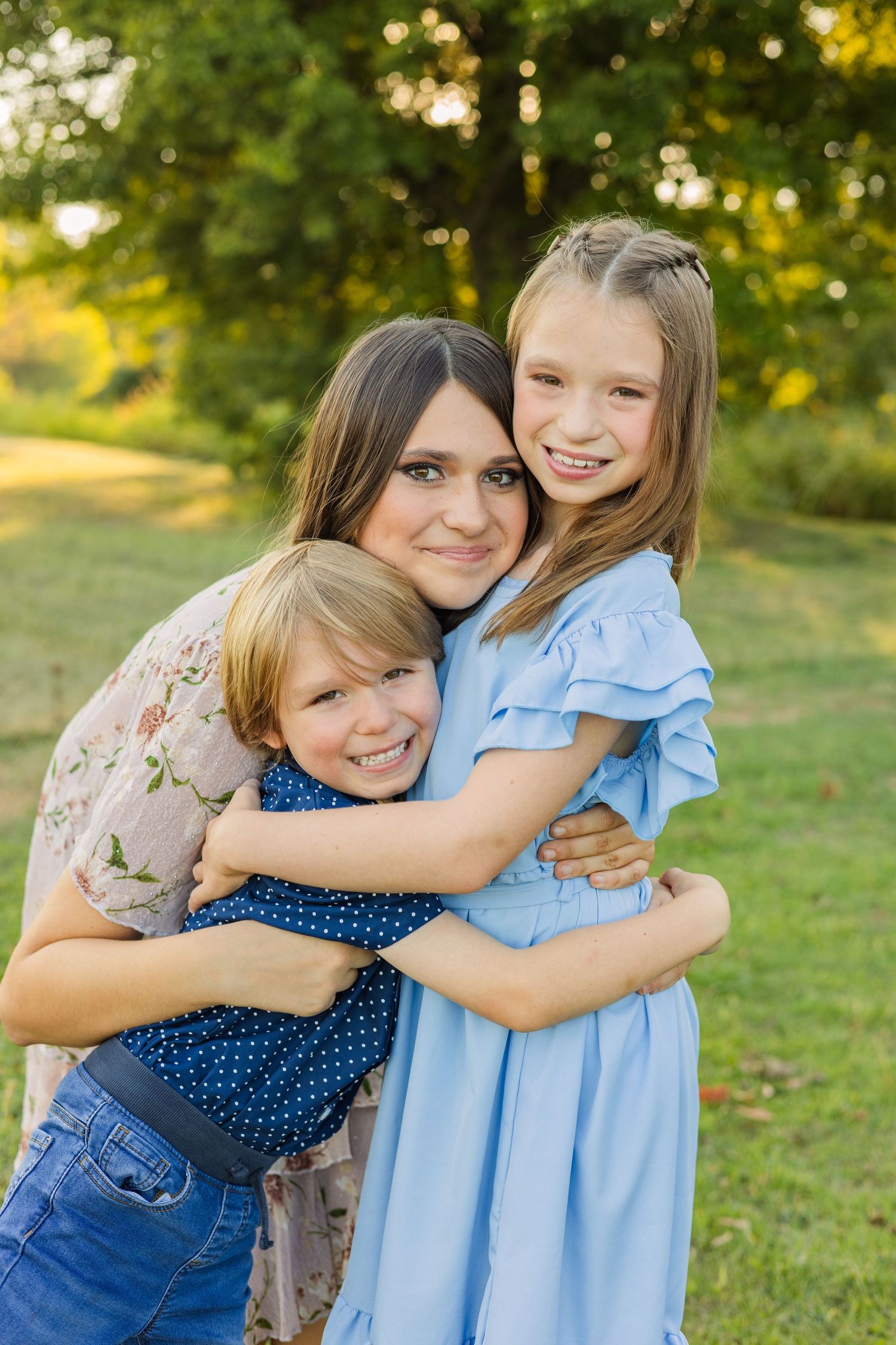 Smiling mother hugging her two children outdoors at golden hour in a warm family portrait.