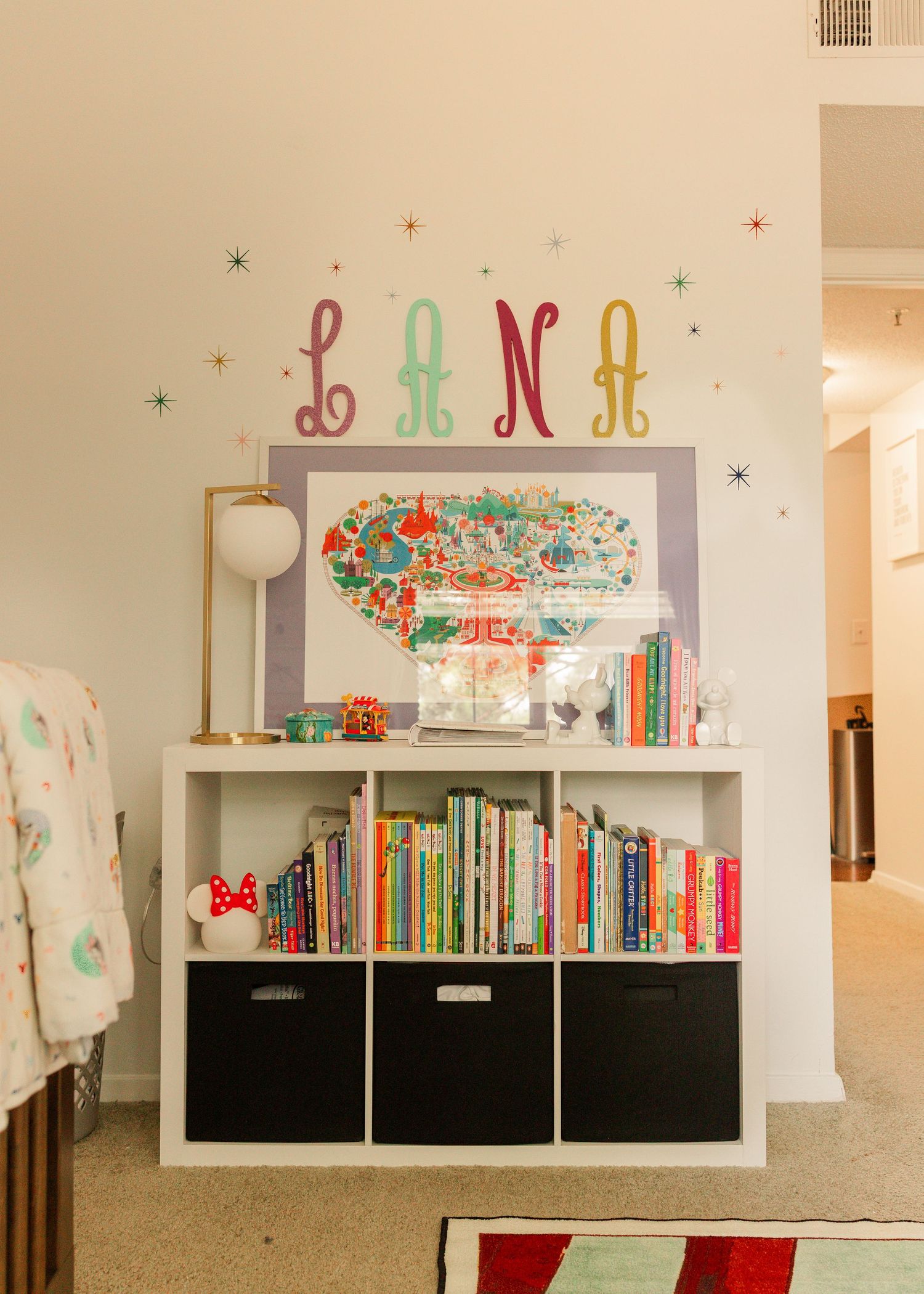 Baby nursery bookshelf with colorful books under wall letters spelling LANA with star decals.