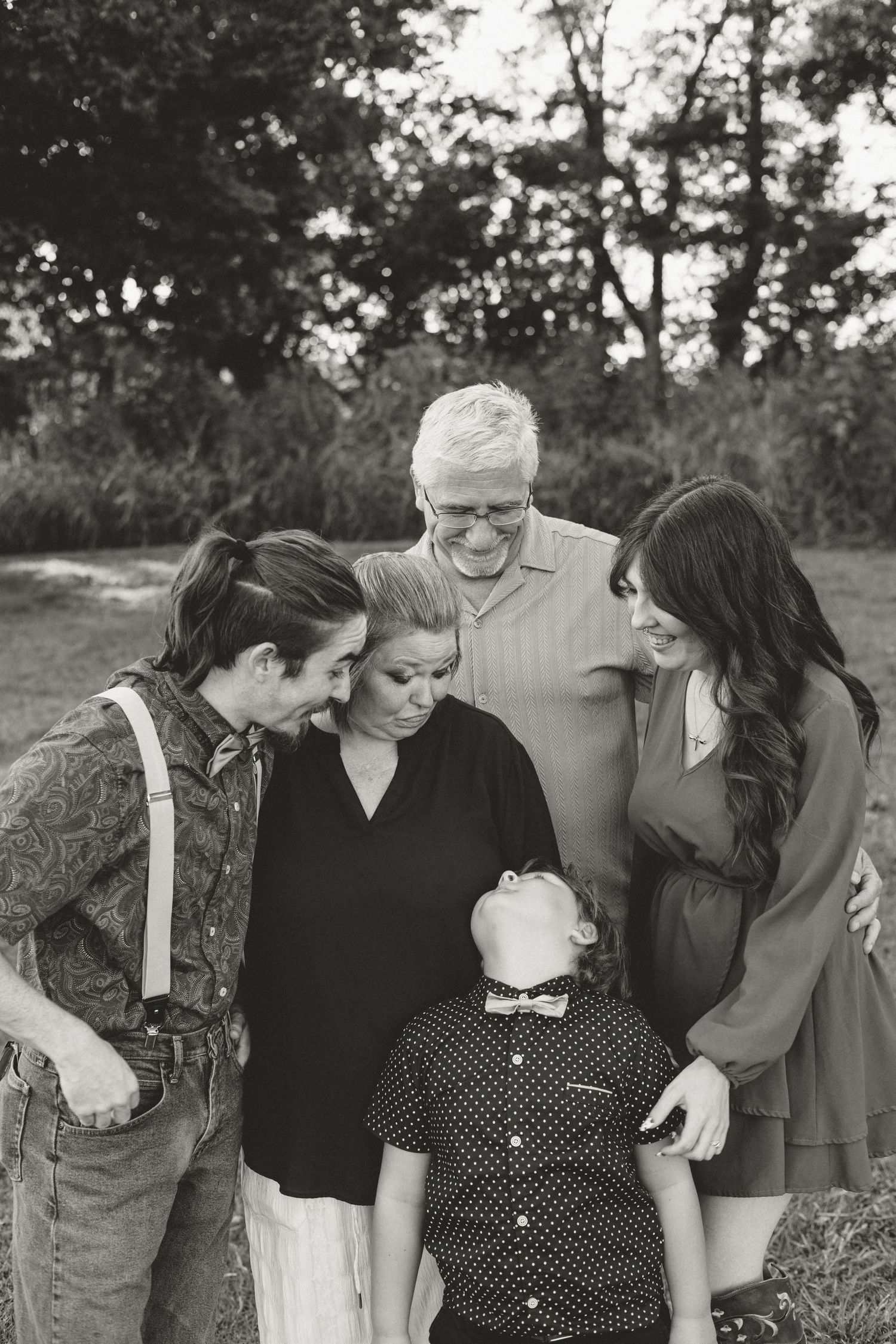 Black and white photo of a multigenerational family gathered closely together outdoors, smiling and looking at a young boy.