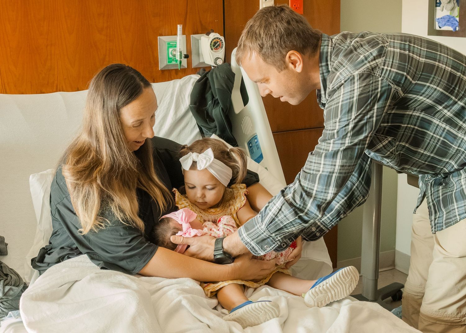 Parents and toddler meeting newborn baby in hospital maternity room.