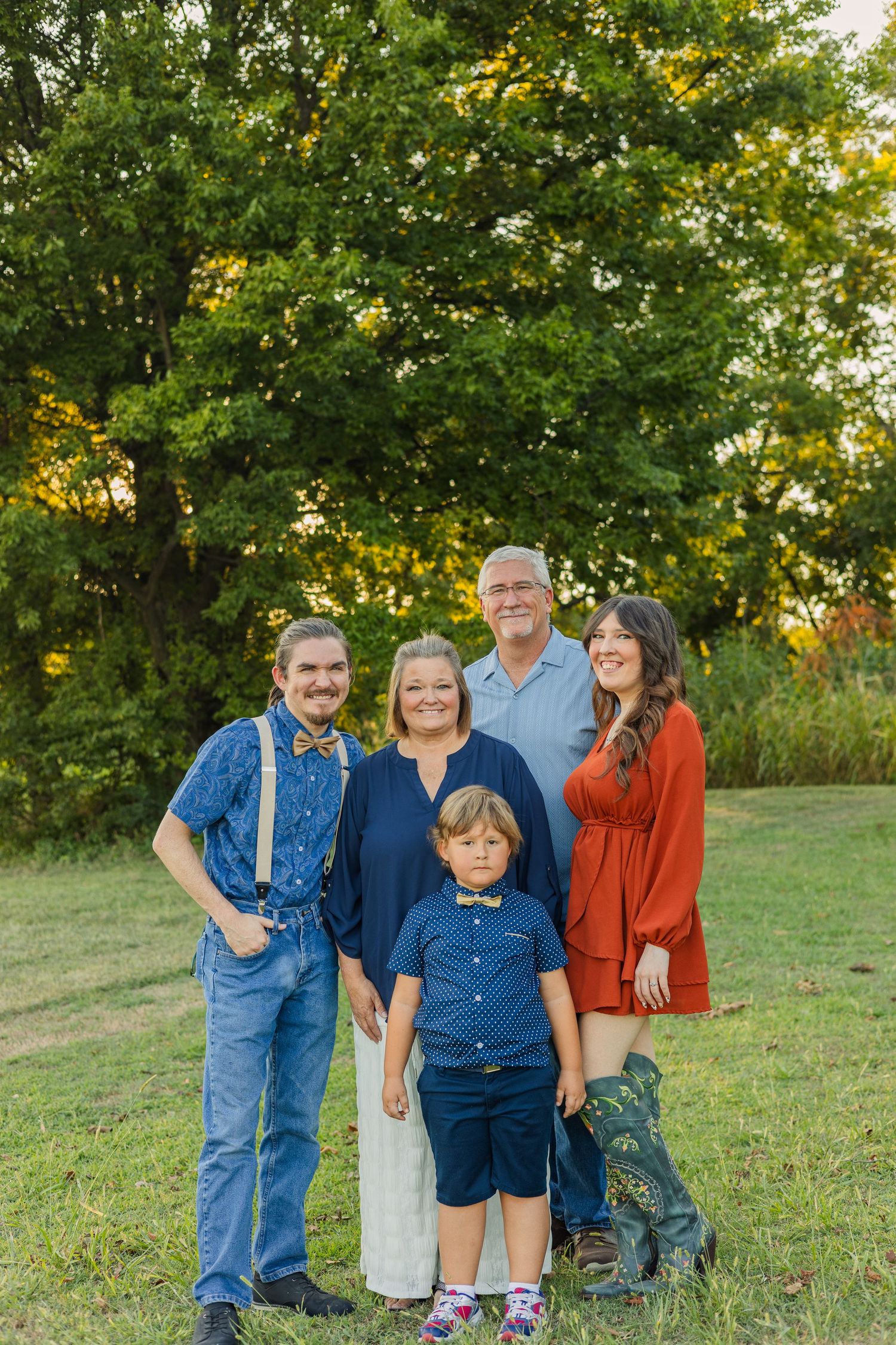 Family of five poses outdoors in a green field during a warm golden hour portrait session.