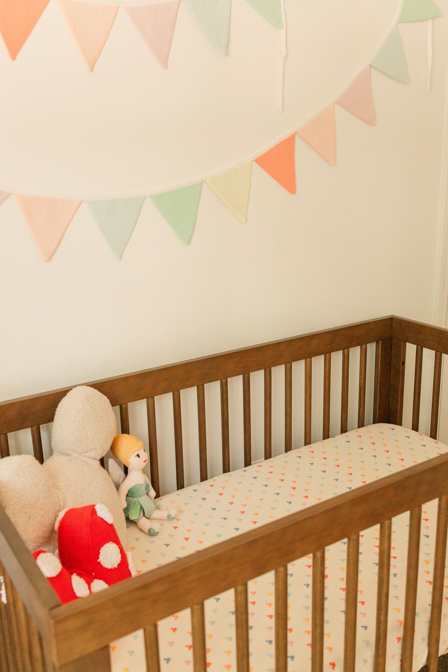 Wooden baby crib with colorful pennant banner, stuffed animals, and Mickey Mouse patterned sheet.