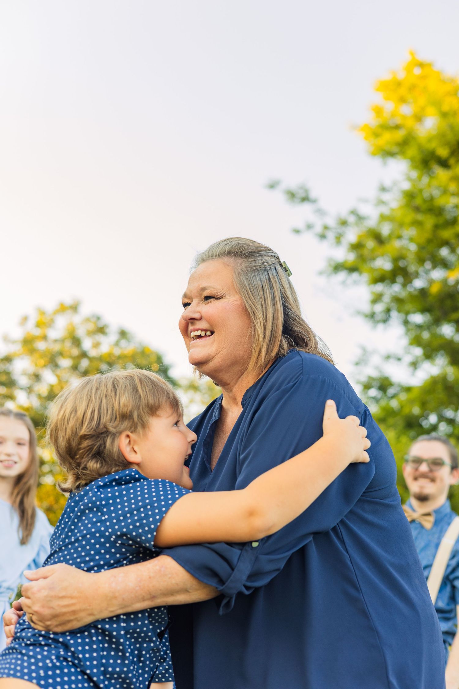 A grandmother laughing joyfully while hugging a young child outdoors during a family photo session.