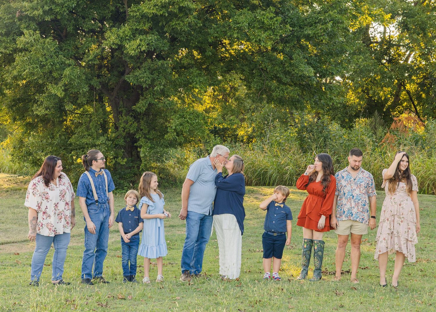 Large extended family portrait outdoors with grandparents kissing in the center surrounded by children and grandchildren.