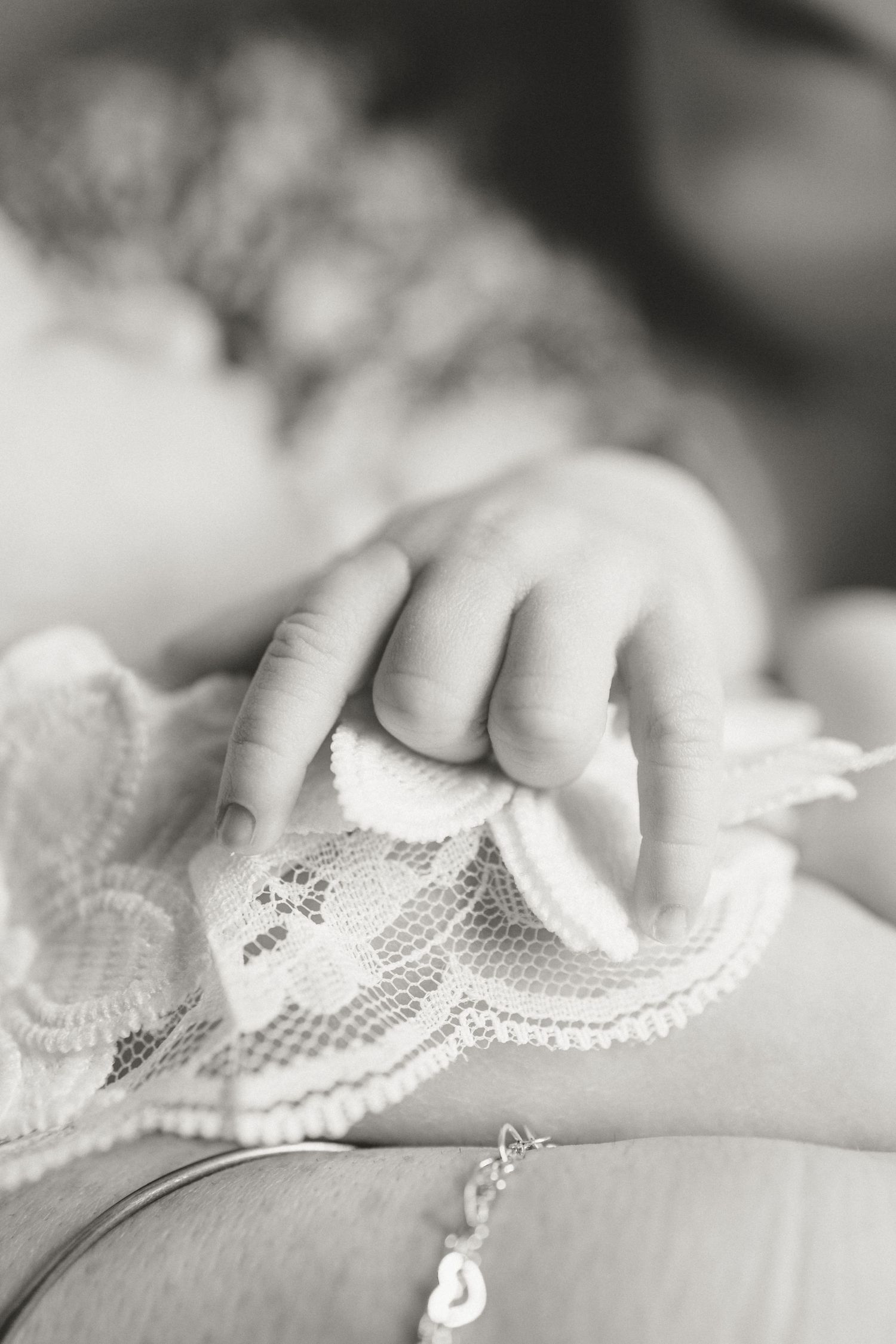 Black and white close-up of newborn babys tiny hand grasping white lace fabric.