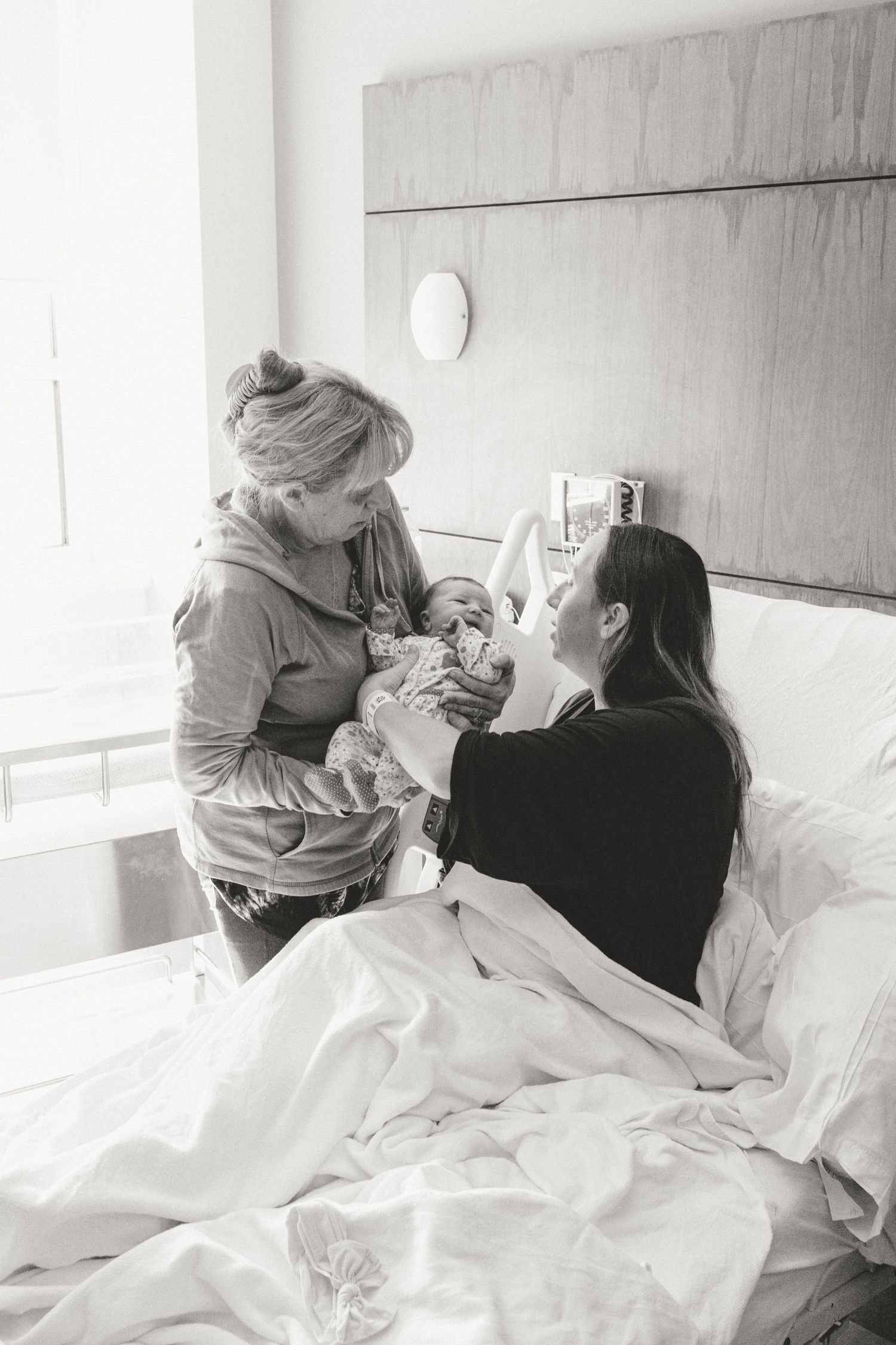 Two women pass a newborn baby in a bright hospital room after birth.