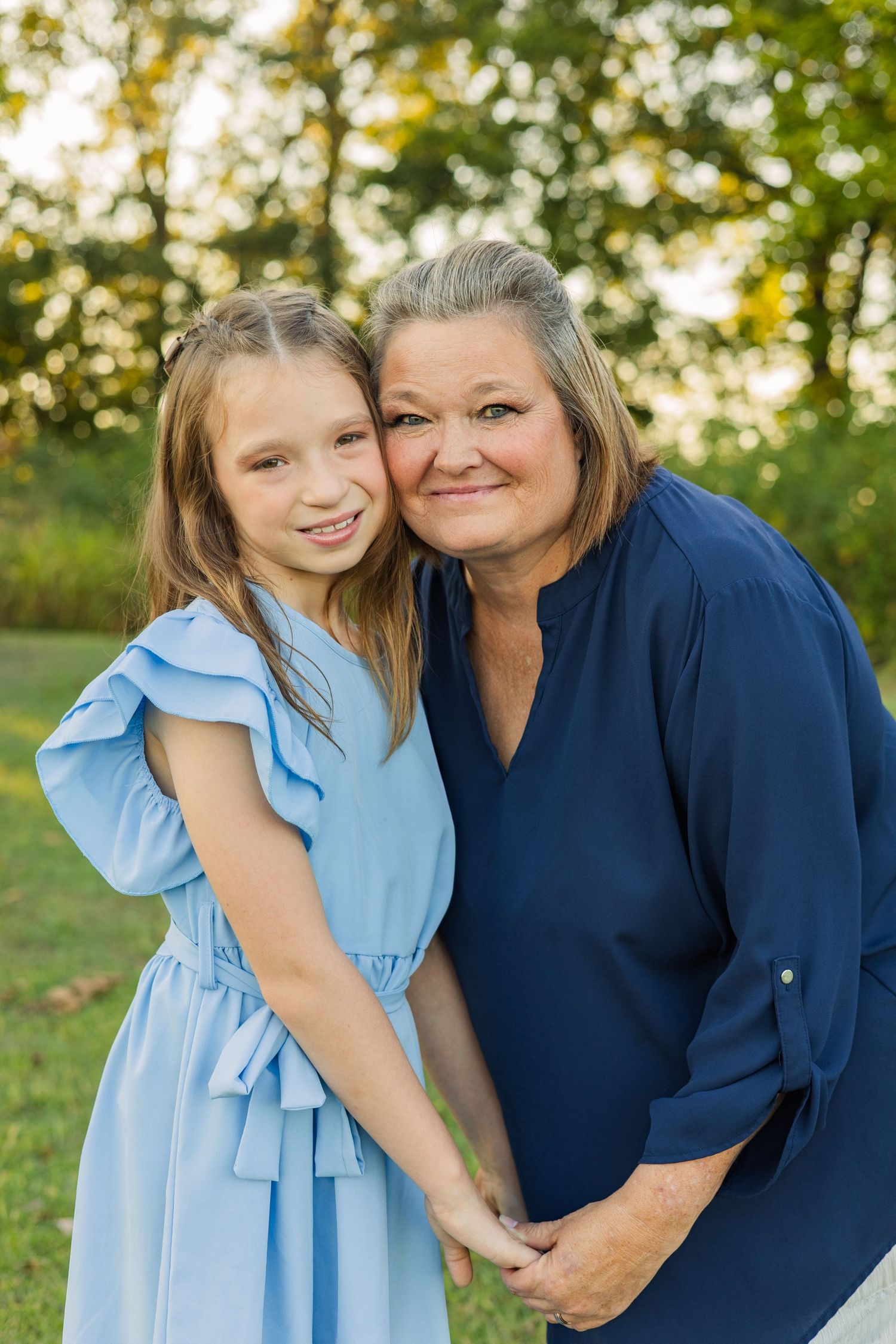 A grandmother in navy blue smiling with a young girl in a blue ruffled dress during outdoor photos.