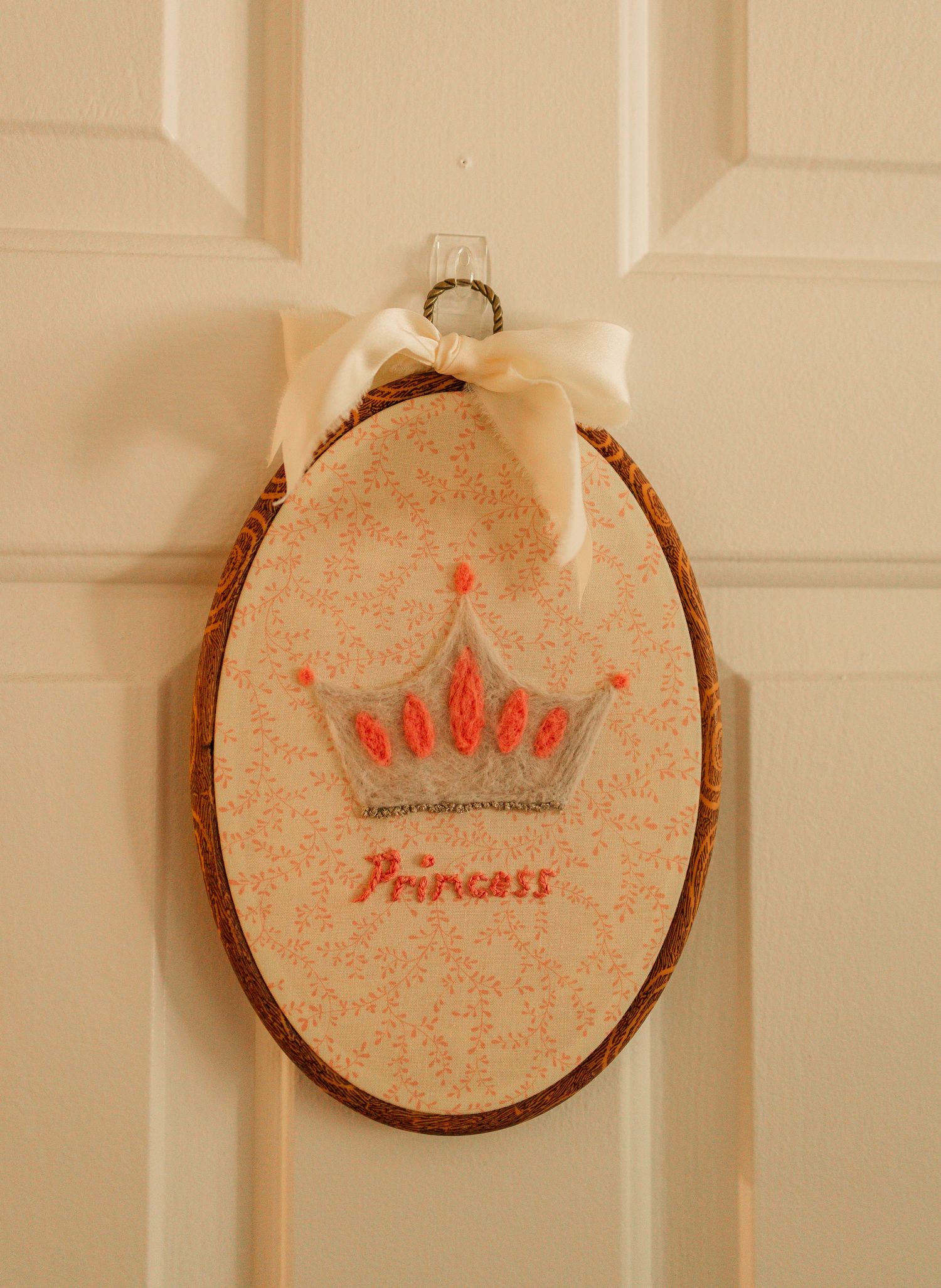 Handmade embroidered oval wood plaque with crown and Princess text hanging on door.