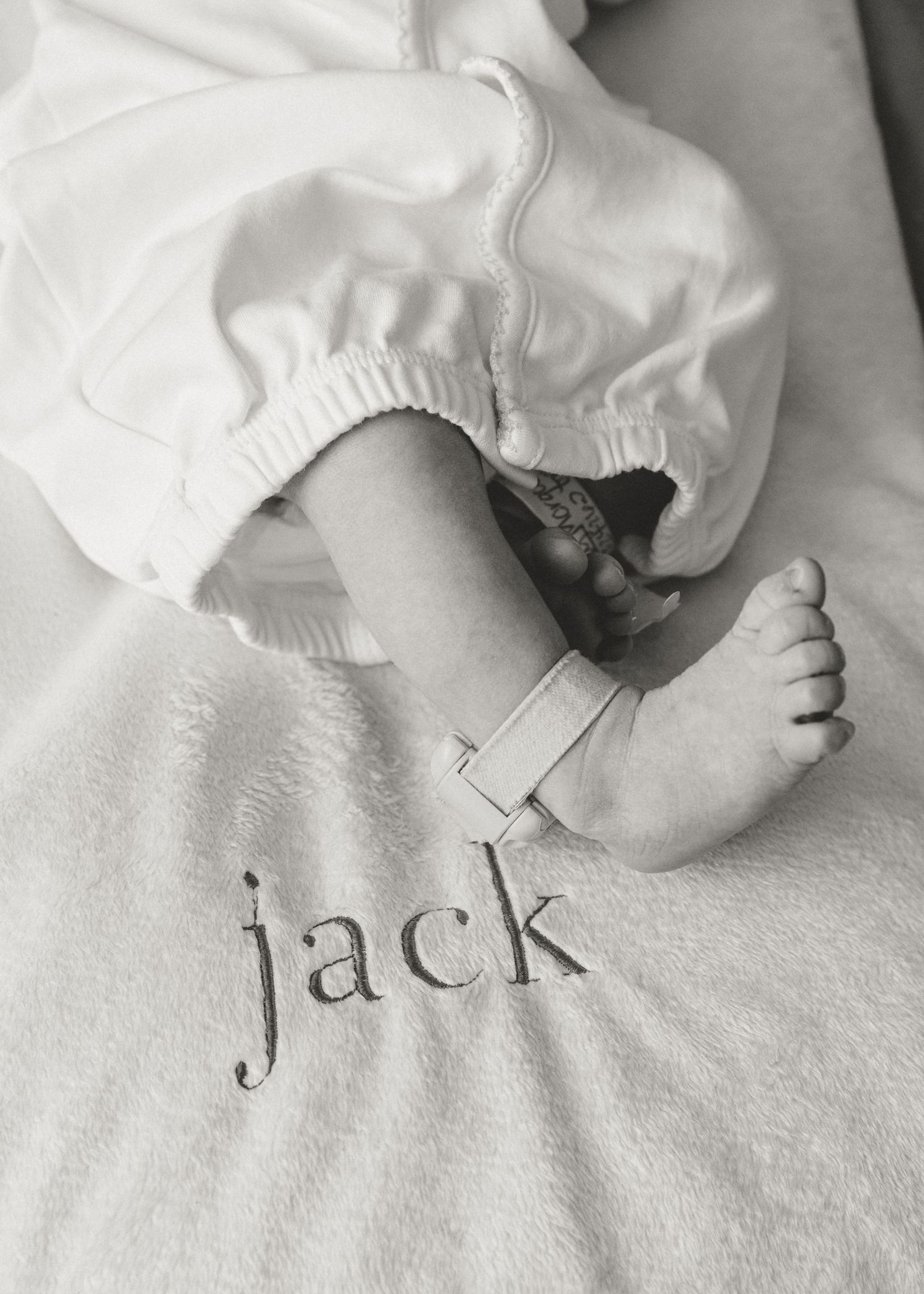 Black and white photo of newborn baby feet with hospital bracelet on blanket reading jack.