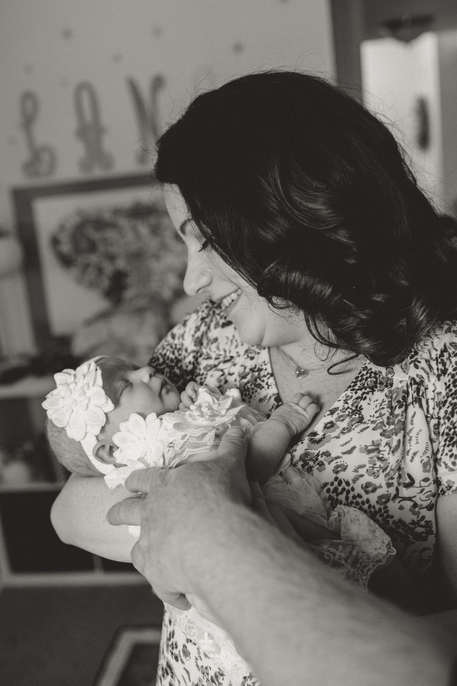 Black and white photo of smiling mother gazing lovingly at her newborn baby in her arms.
