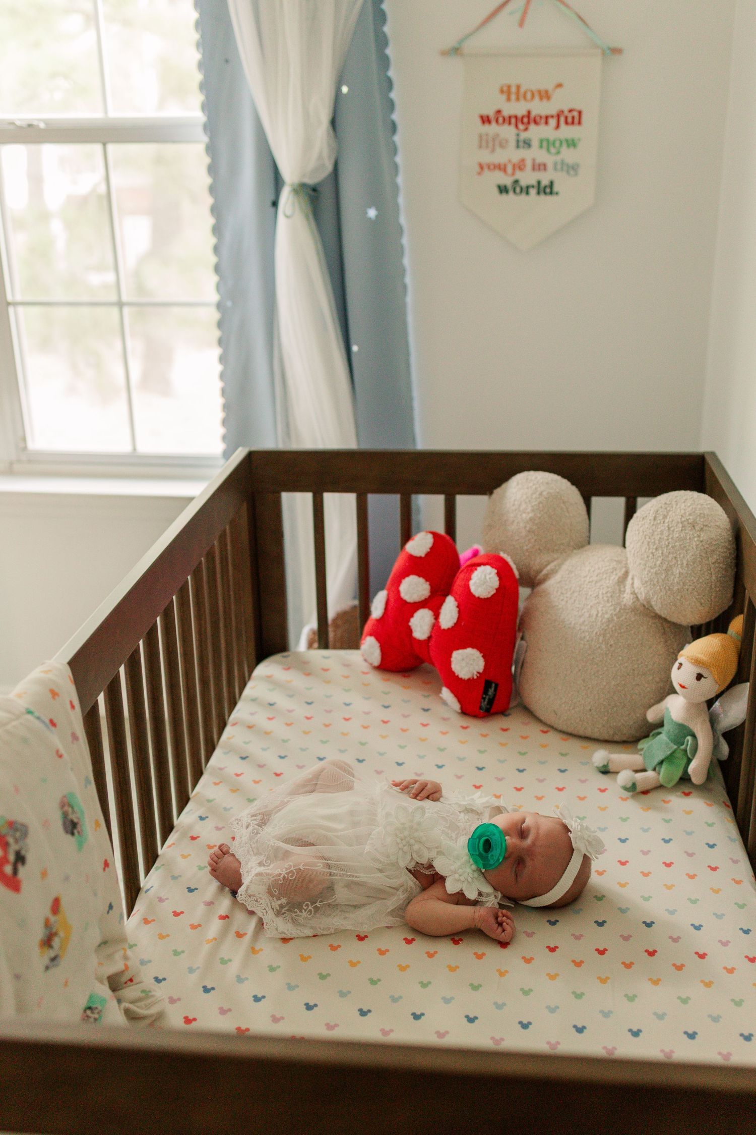 Newborn baby sleeping in a dark wood crib with Mickey Mouse themed bedding and plush toys.