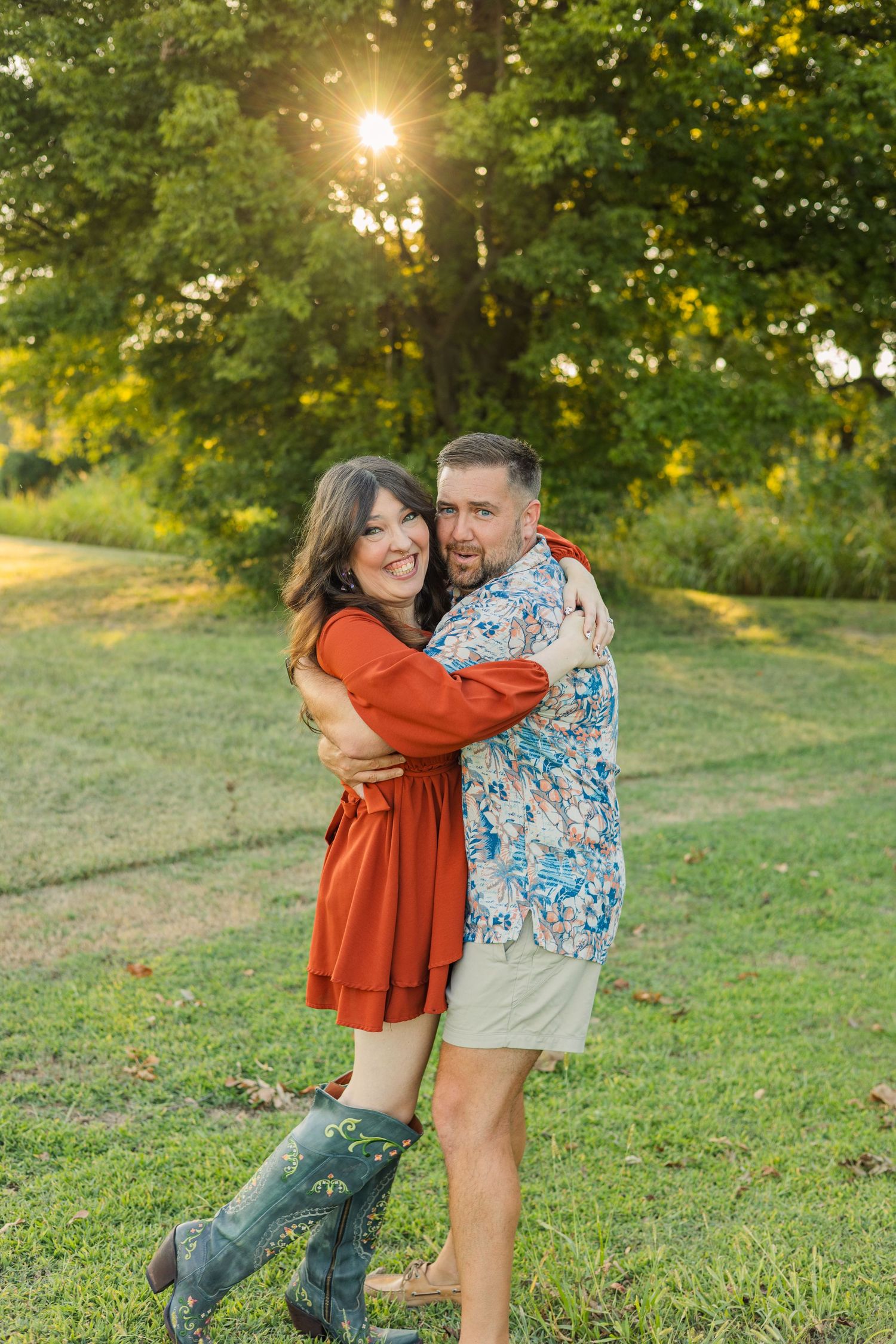 Joyful couple embracing in a sunny park, woman in red dress with green boots, man in floral shirt.
