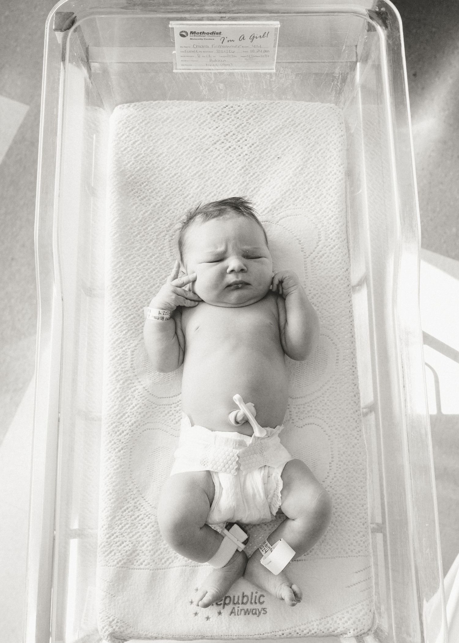 Overhead black and white photo of newborn baby in hospital bassinet.