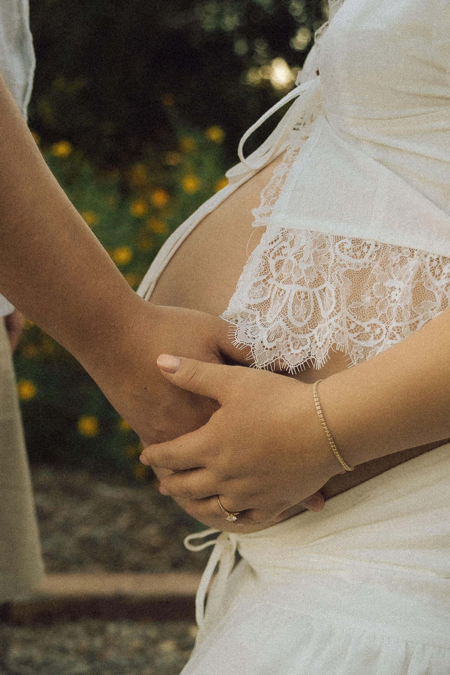 Close-up of a pregnant woman in white lace dress with hands gently cradling her baby bump.