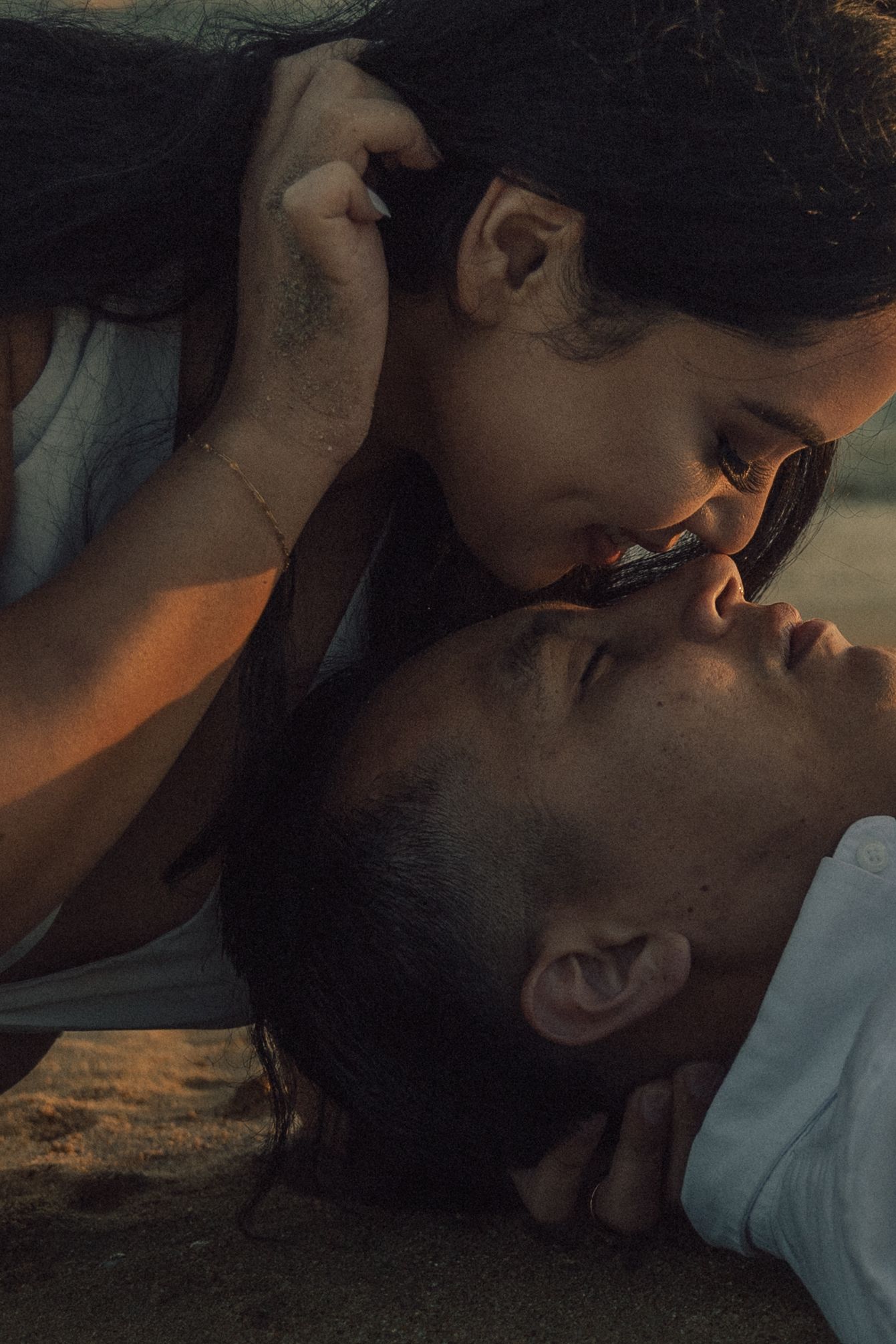 Romantic close-up of a couple almost kissing on the beach at warm golden hour light.