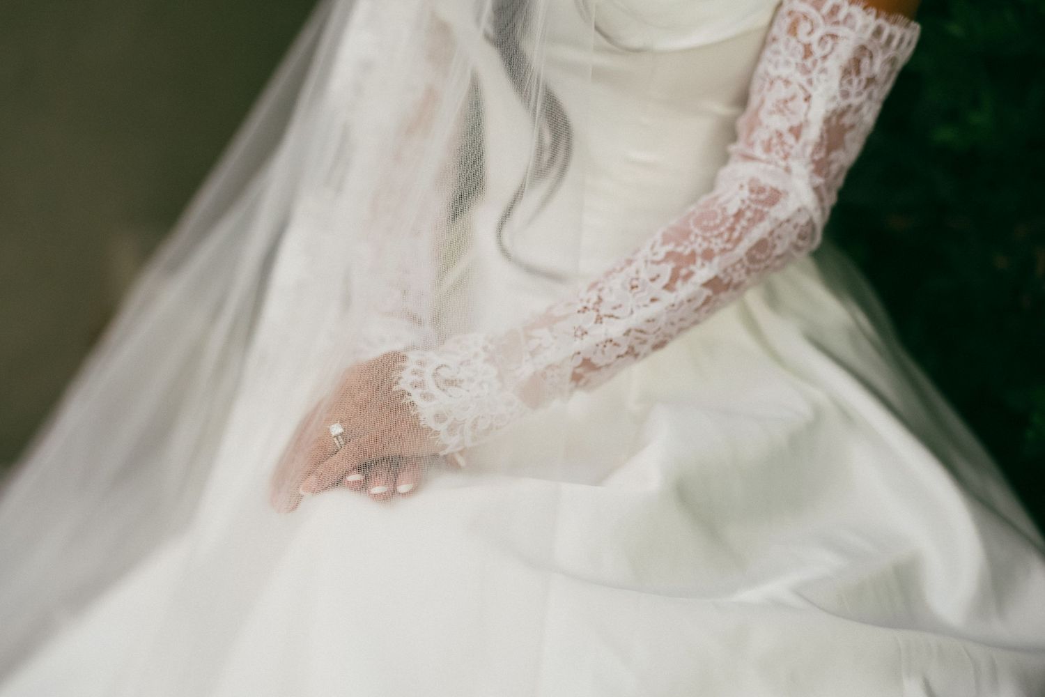 Close-up of bride wearing elegant white lace long gloves with flowing veil and wedding gown detail.
