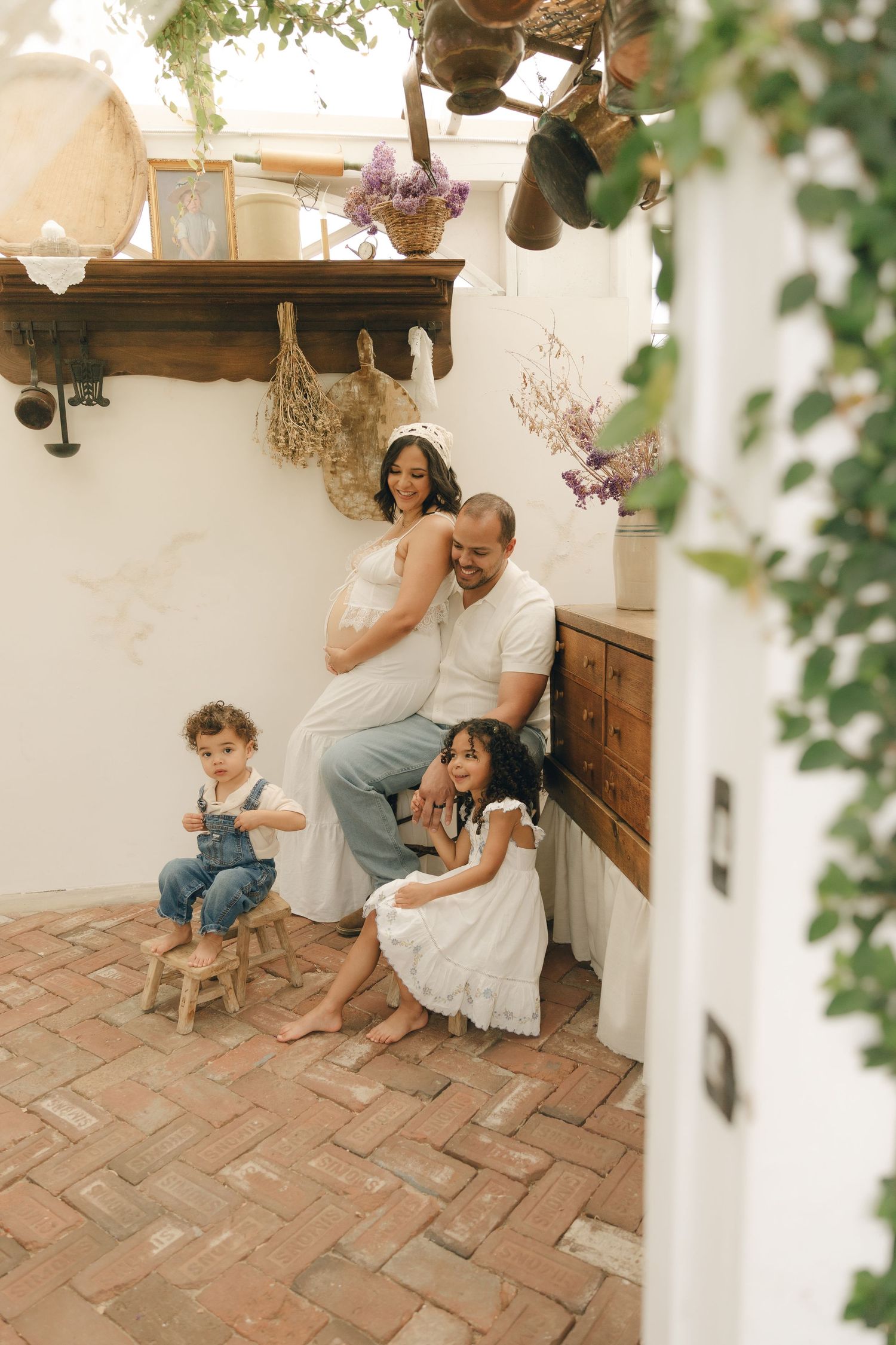 Happy family with pregnant mother, father, and two children pose in a rustic brick-floored studio.