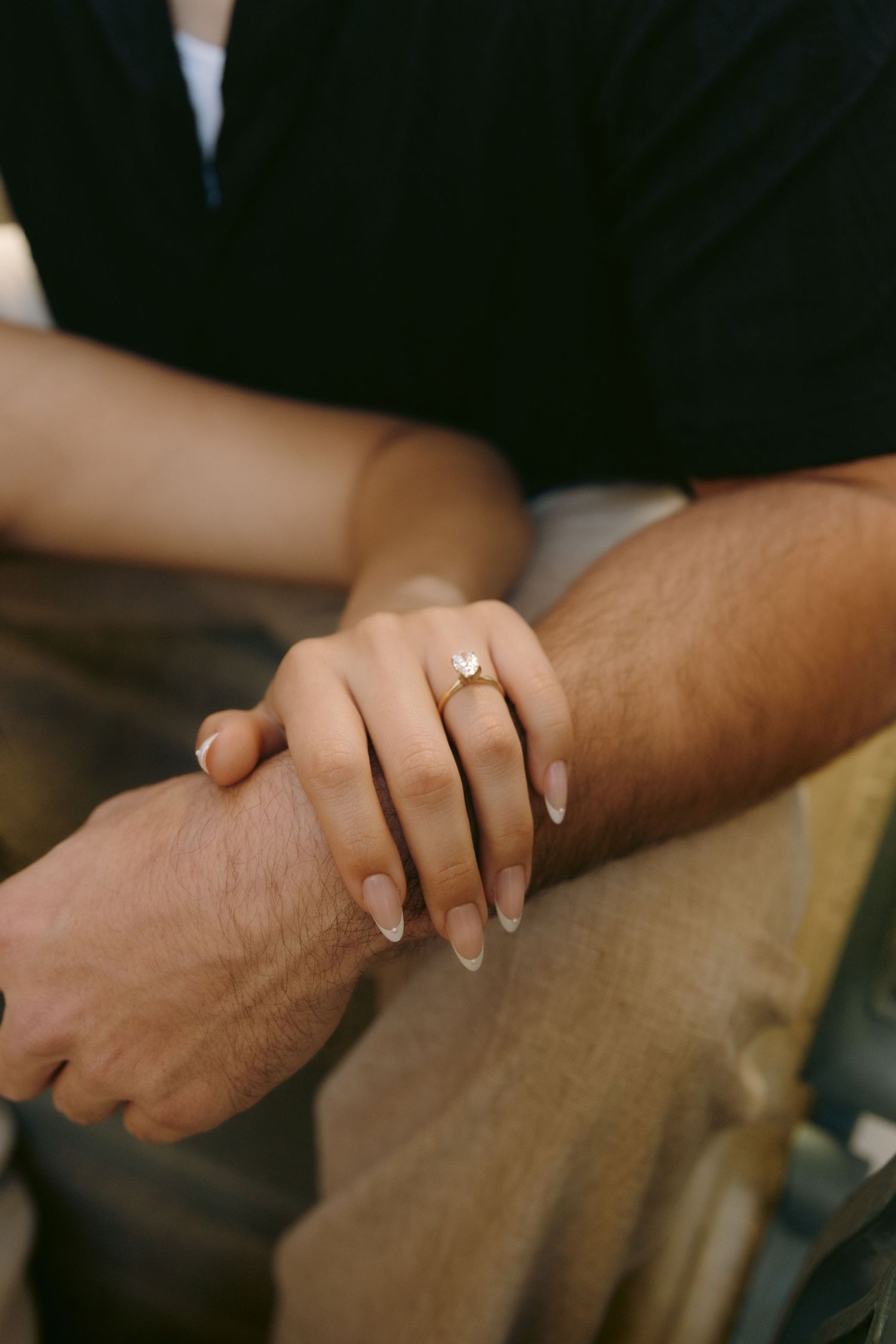 Close-up of couple holding hands showing womans gold engagement ring with heart-shaped diamond stone.
