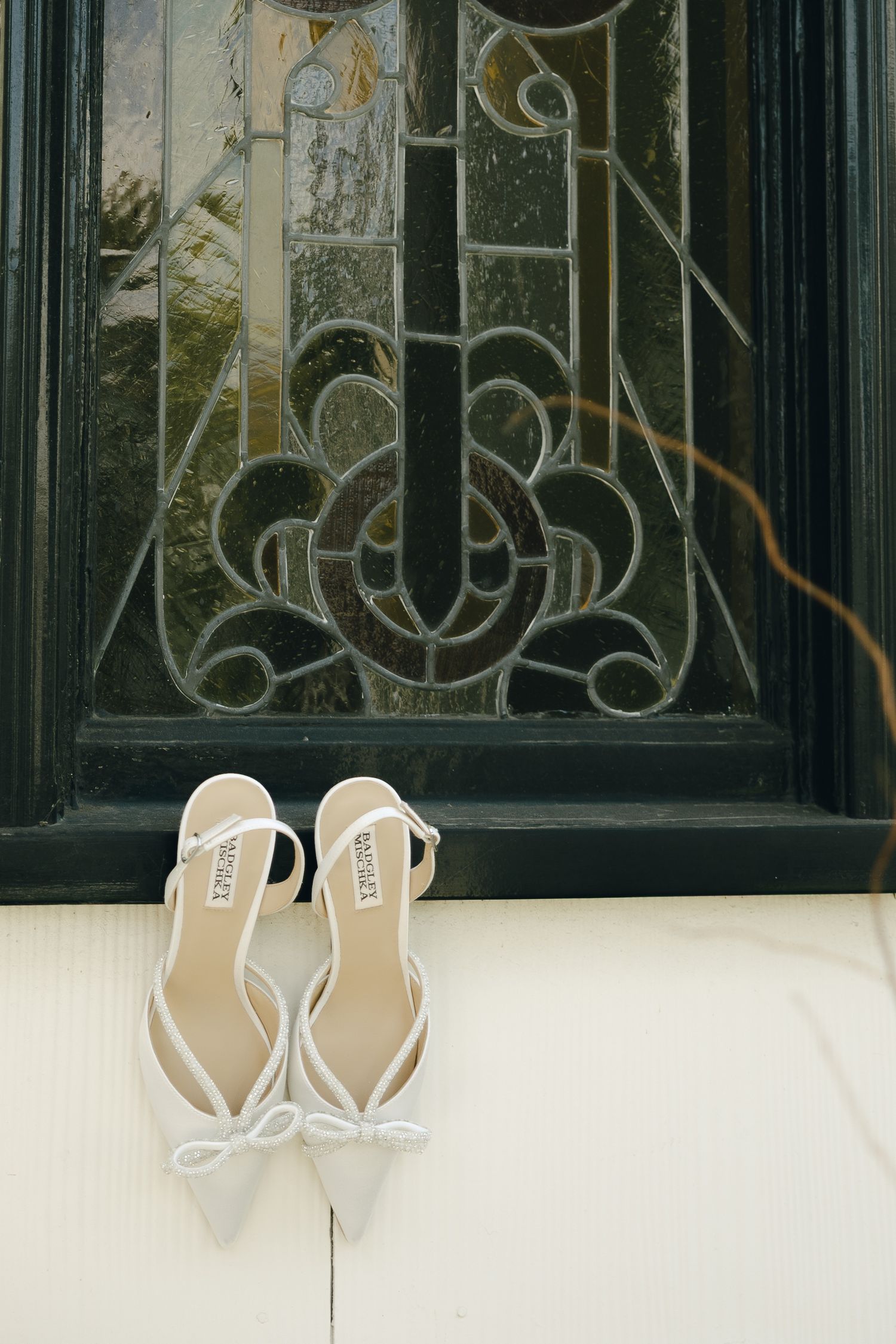White bridal heels with bow detail placed in front of an ornate stained glass door.