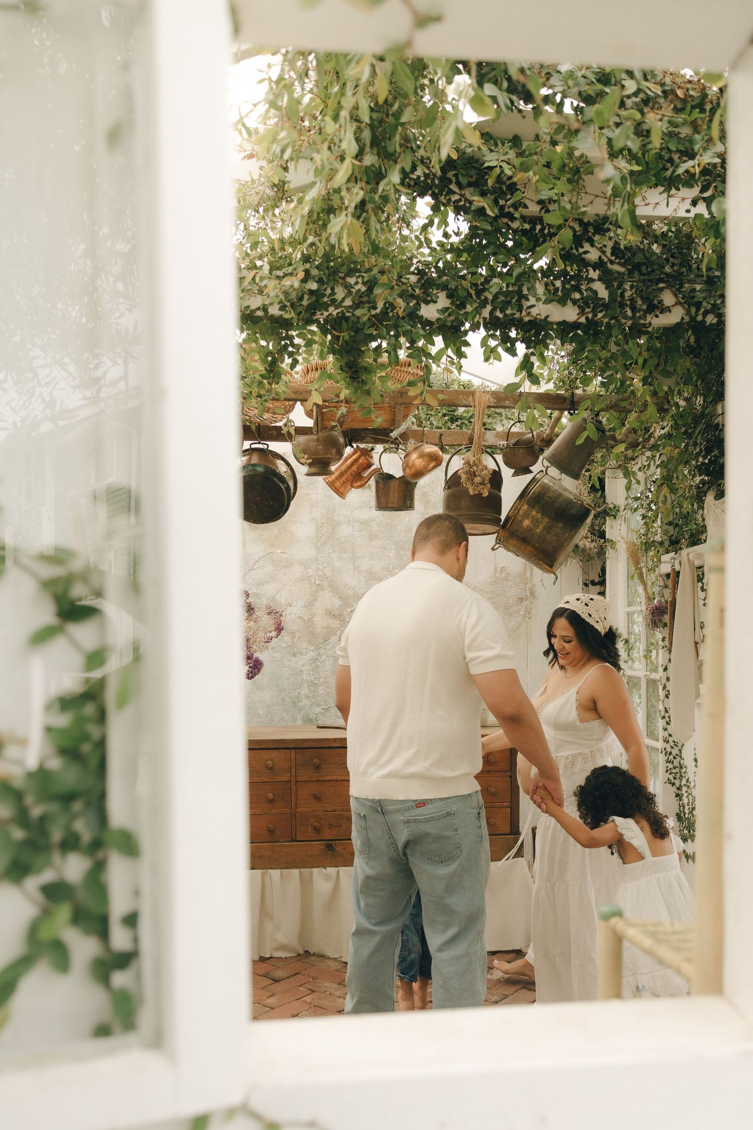 Father in white shirt dances with young daughter in charming outdoor garden space with hanging pots.