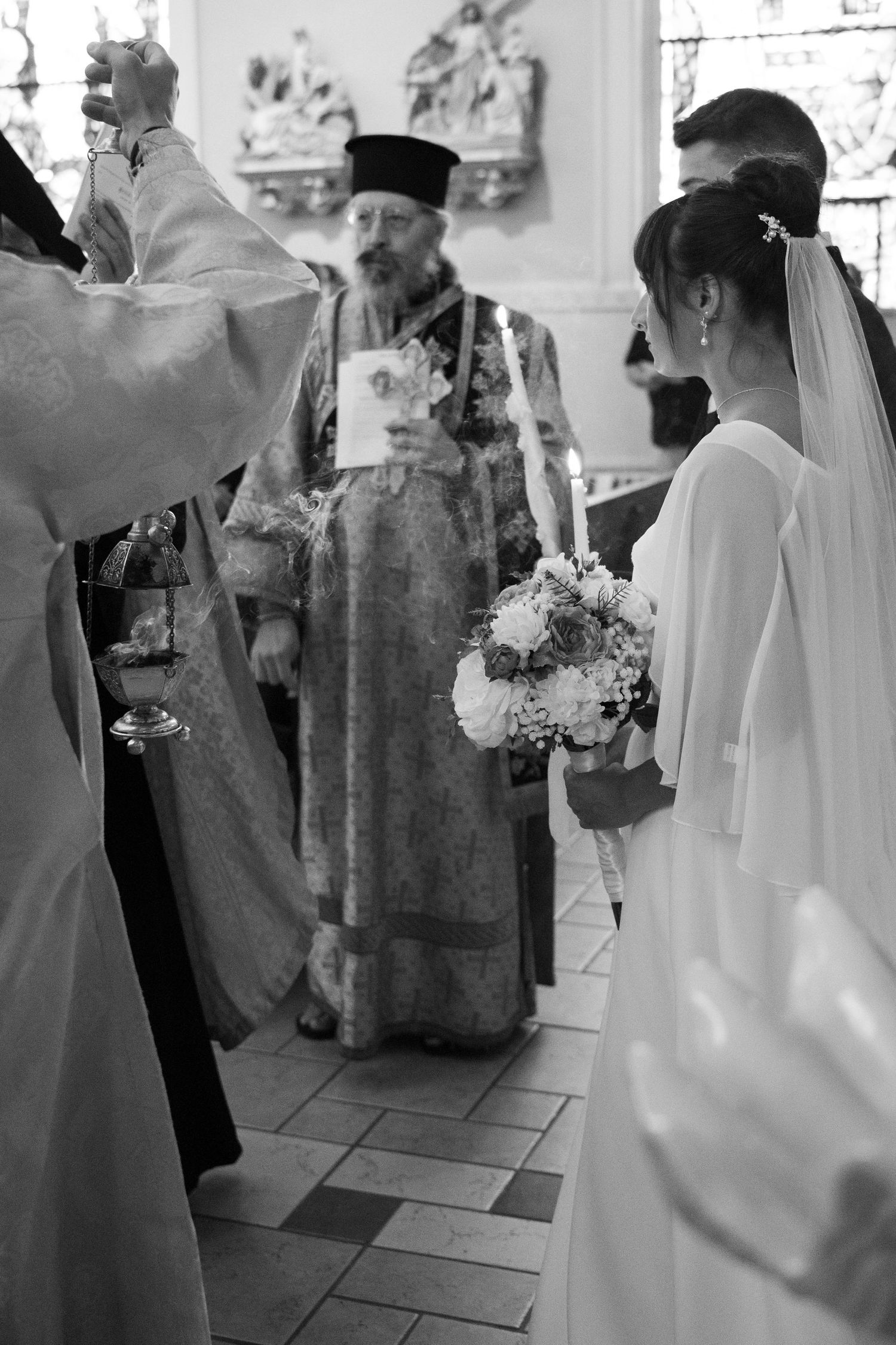 Black and white photo of a bride holding flowers during an Orthodox Christian wedding ceremony.