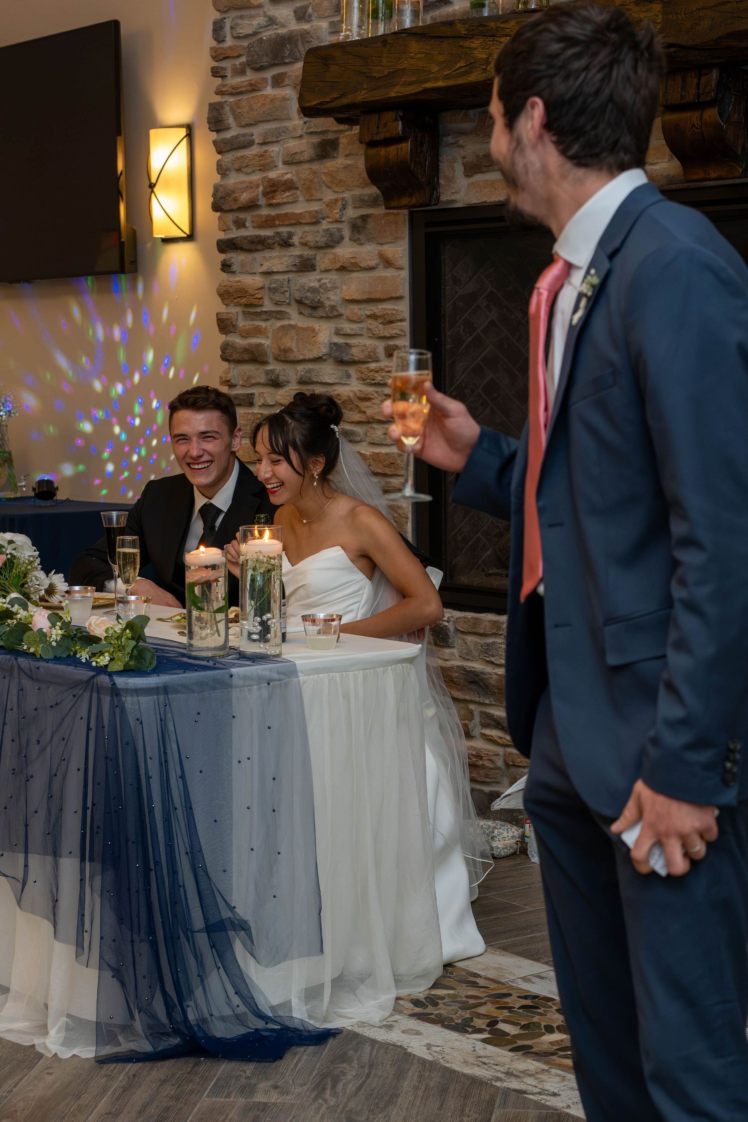 Best man giving champagne toast to smiling bride and groom at wedding reception.