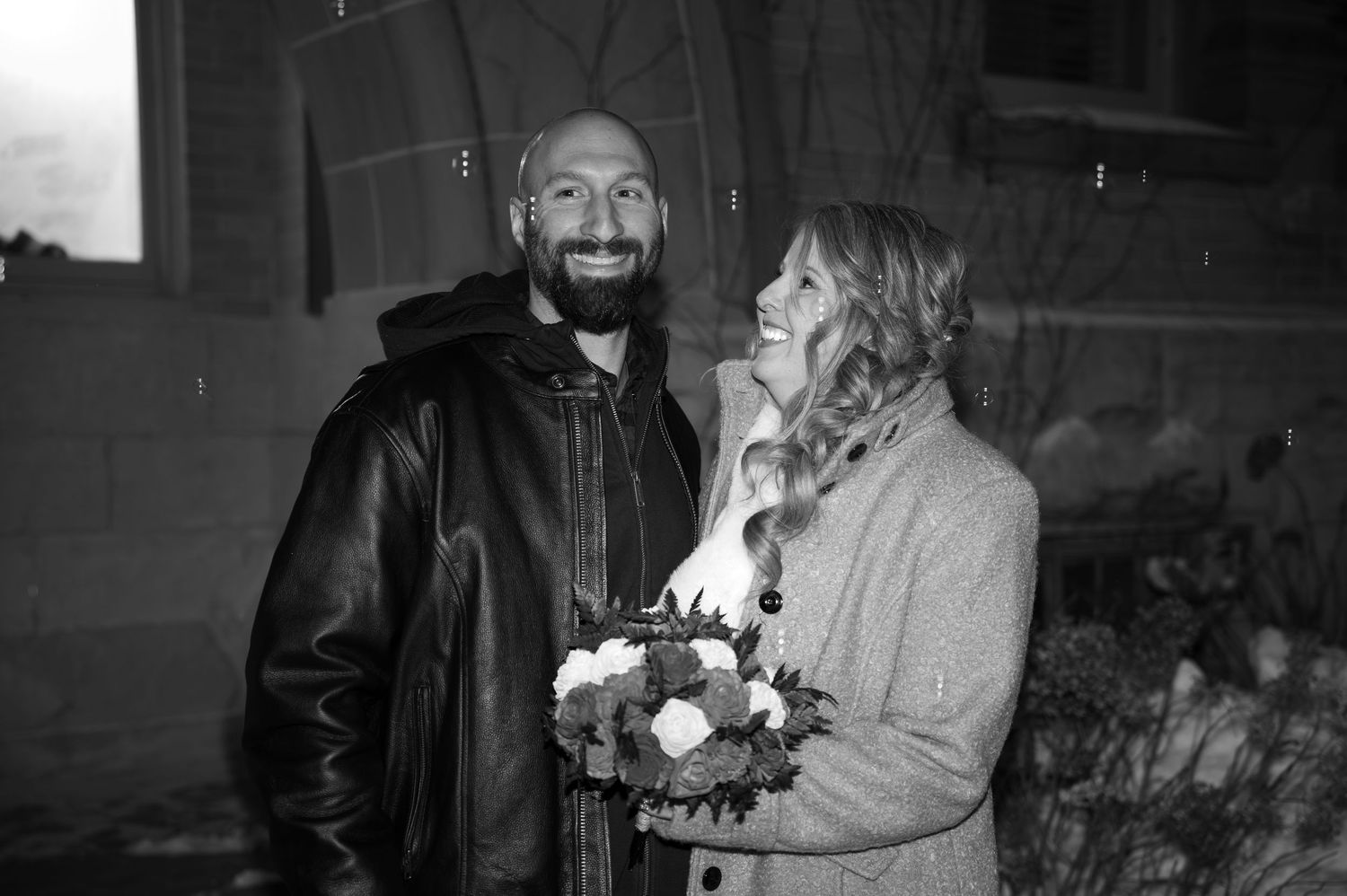 Happy couple standing in the rain holding a floral bouquet in black and white photo.