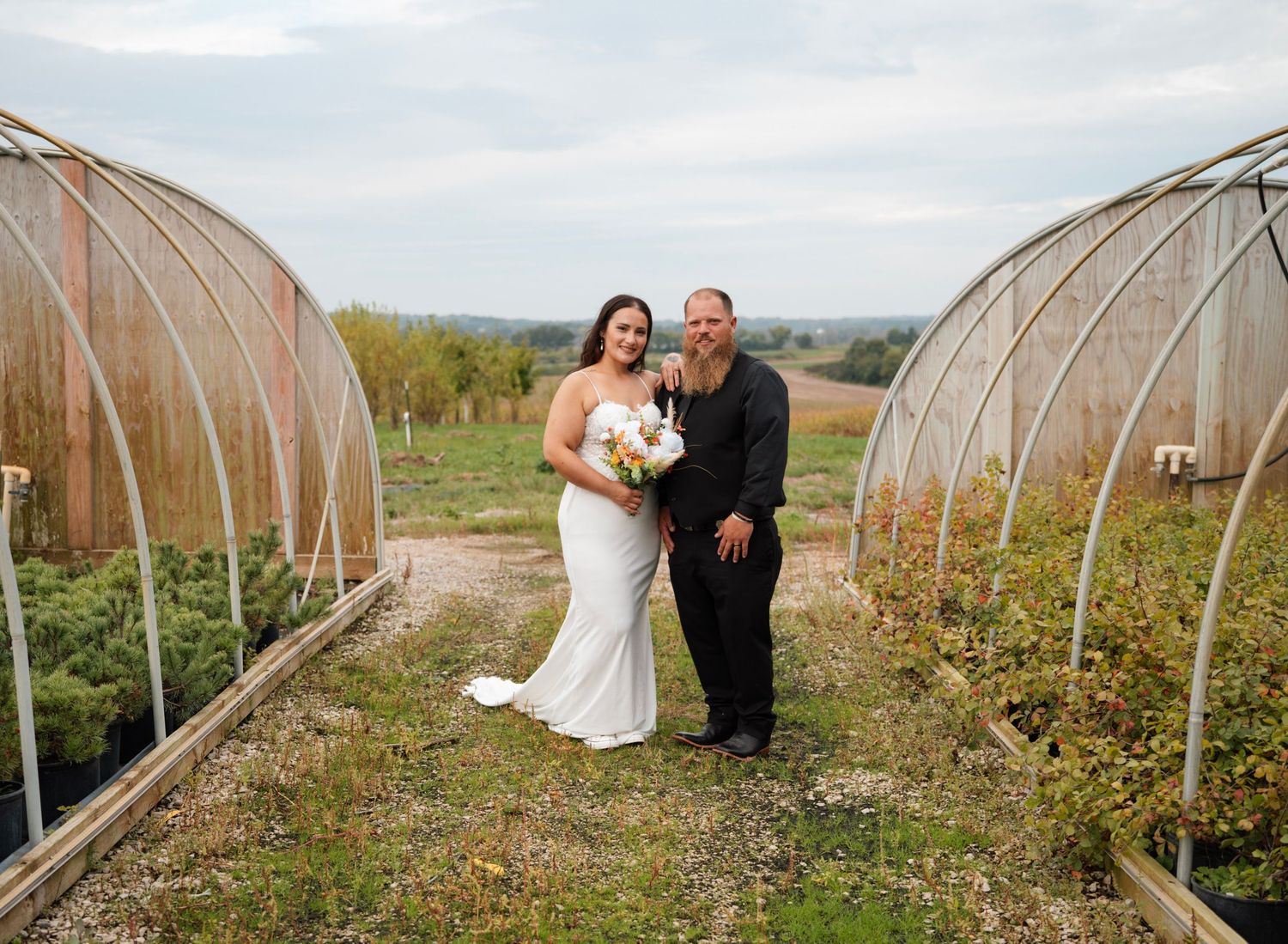 Bride and groom standing between greenhouse tunnels on a farm wedding venue.