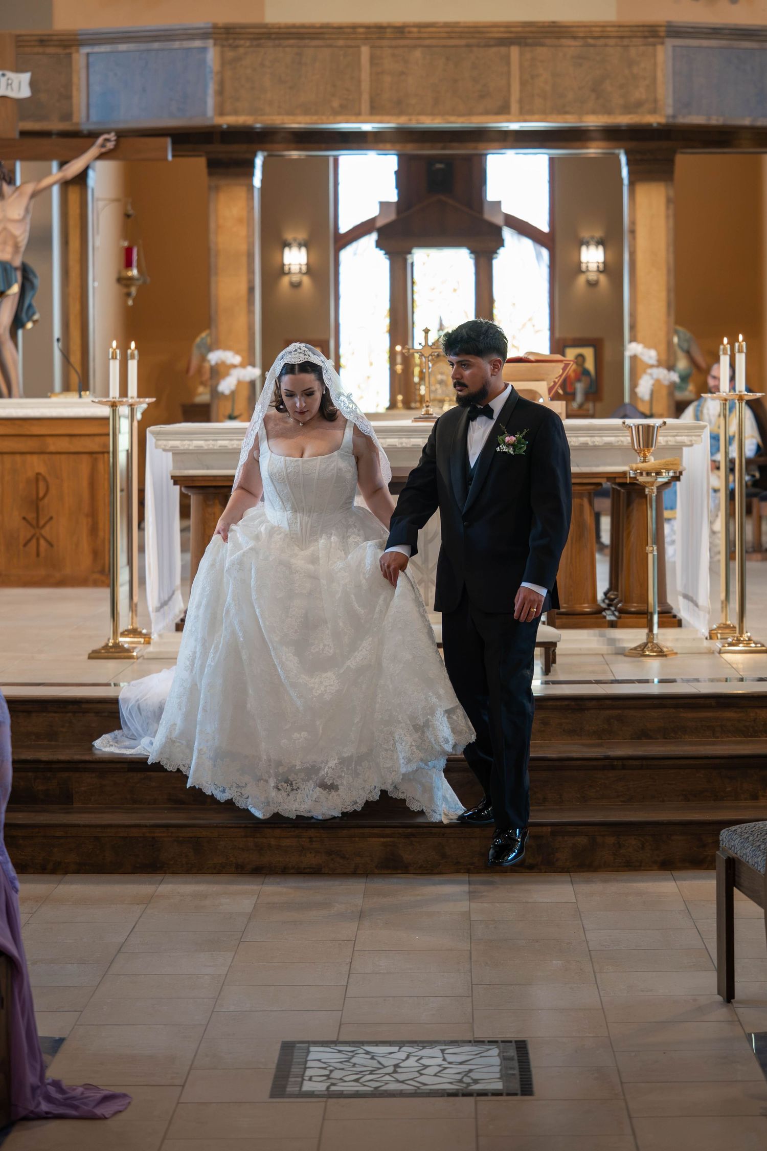 Newlywed couple descends altar steps hand in hand following their Catholic church wedding ceremony.