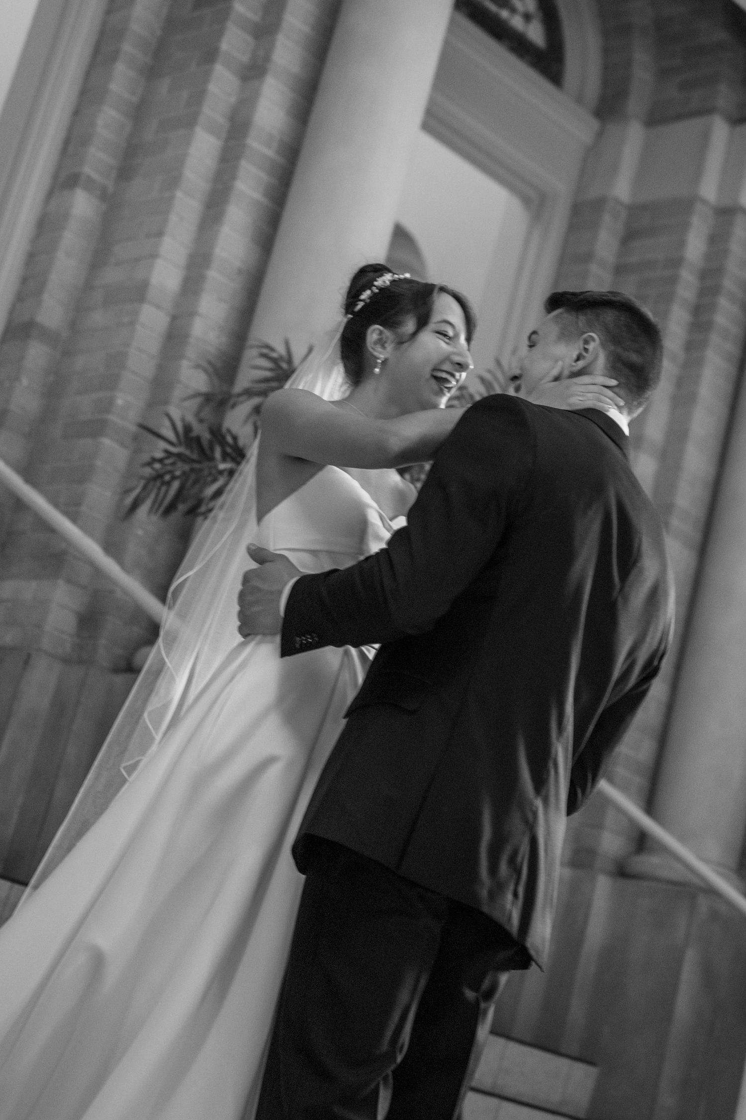 Black and white photo of bride and groom sharing joyful first look moment outside church.