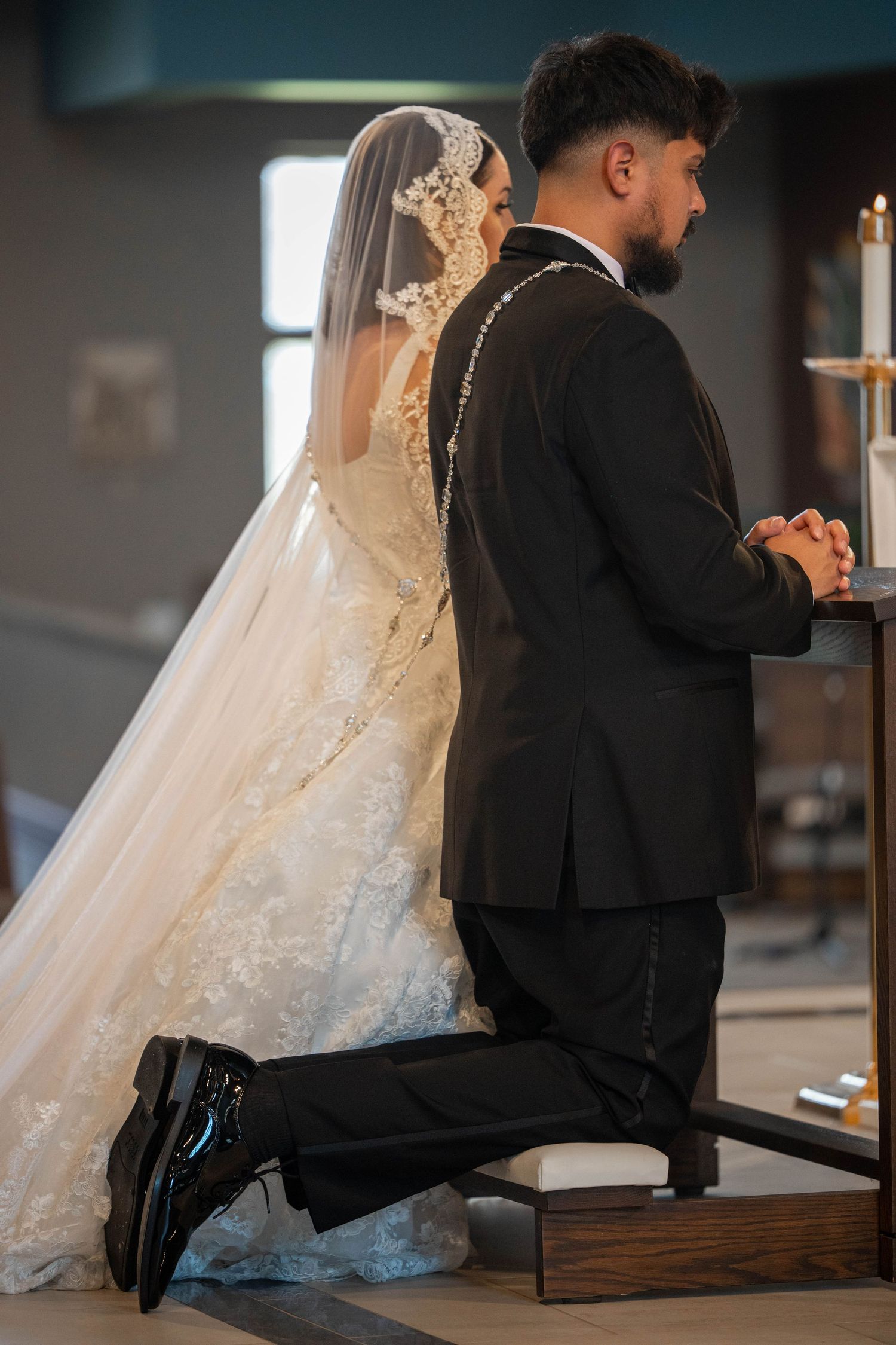 Bride and groom kneel together in prayer during church wedding ceremony.