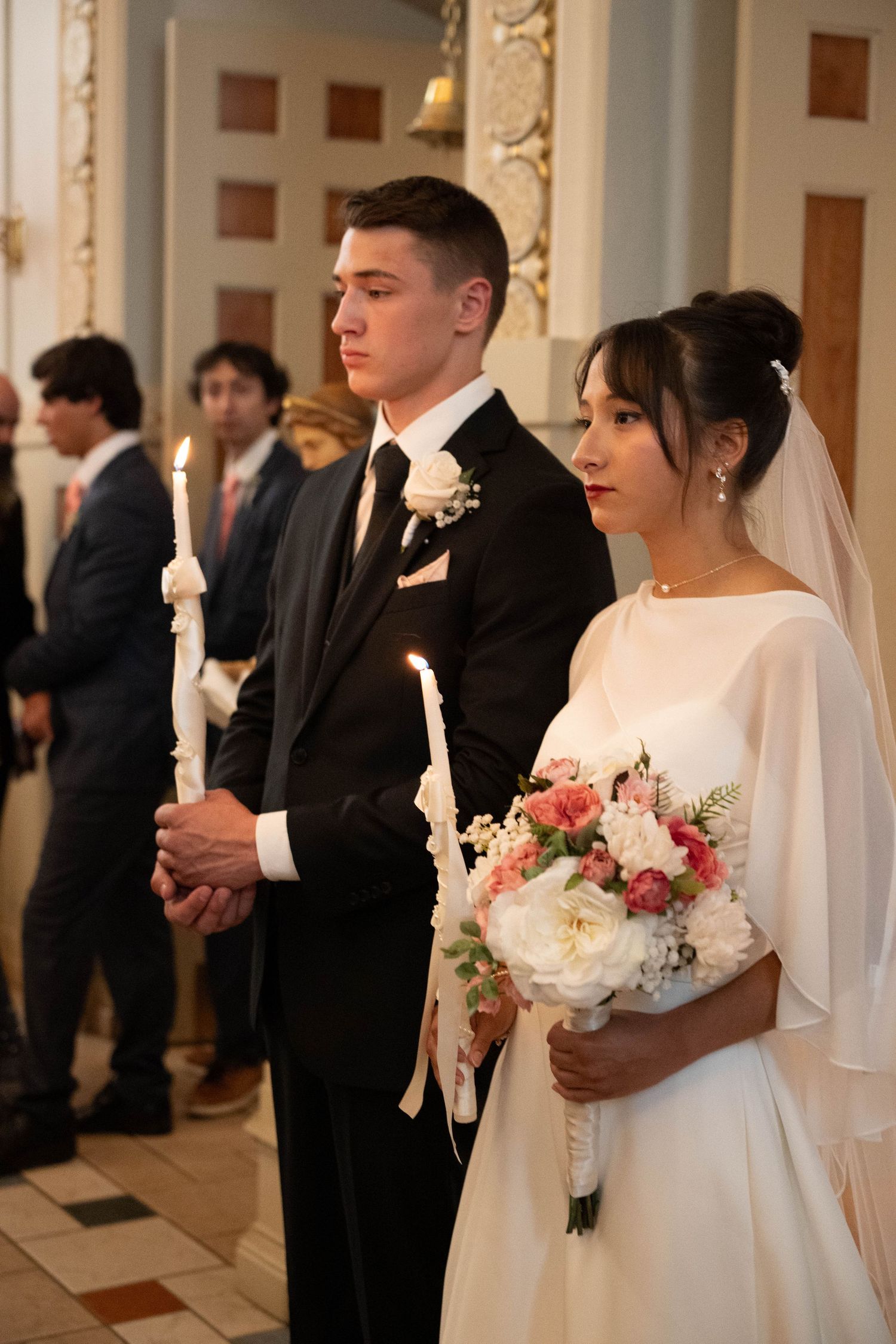 Bride and groom holding candles and a floral bouquet during a church wedding ceremony.