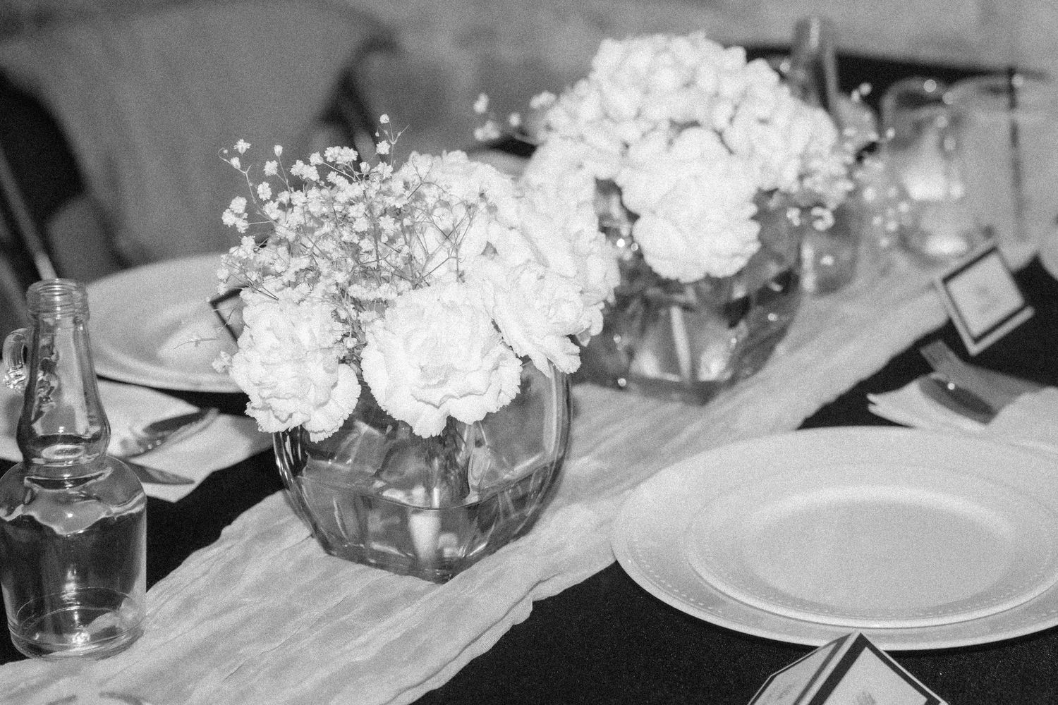 Black and white photo of wedding reception table with white rose and hydrangea floral centerpieces.