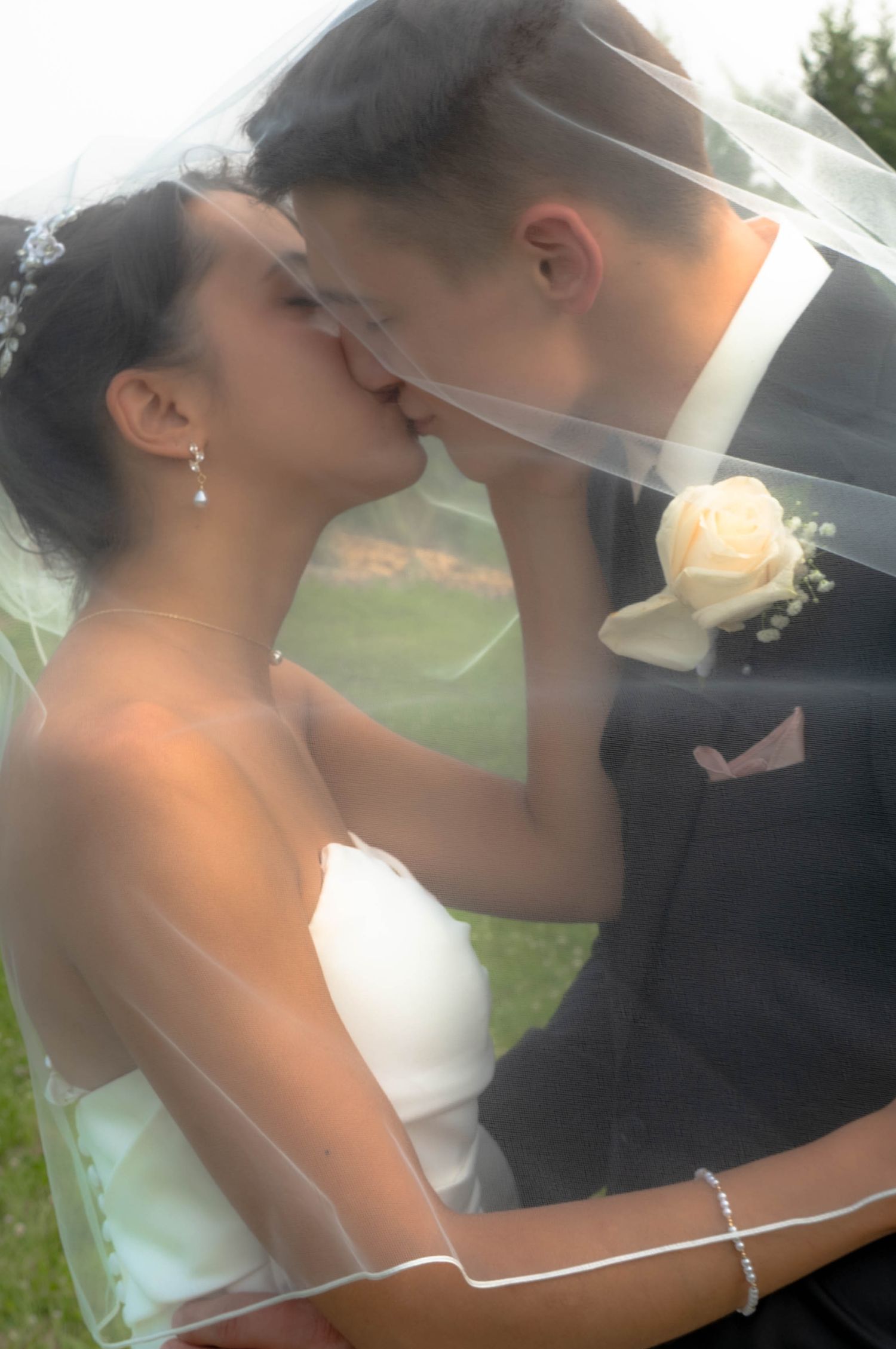 Romantic bride and groom sharing kiss under flowing white veil on wedding day.