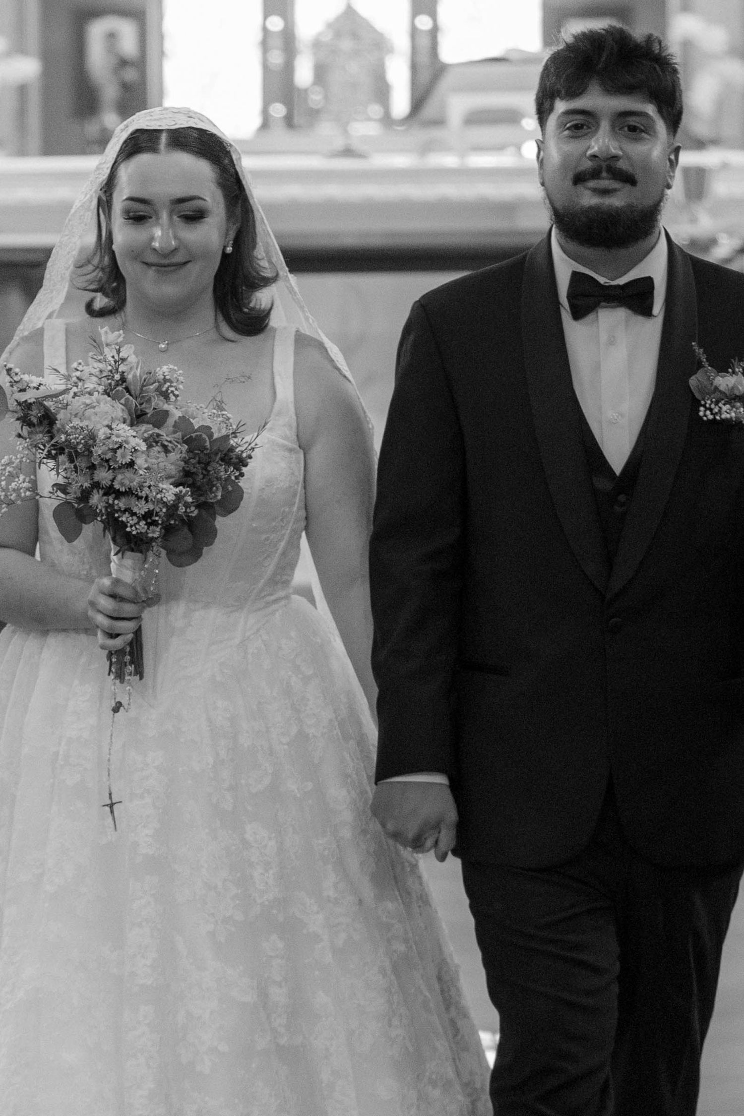 Bride and groom walk hand in hand in black and white wedding photo outdoors.
