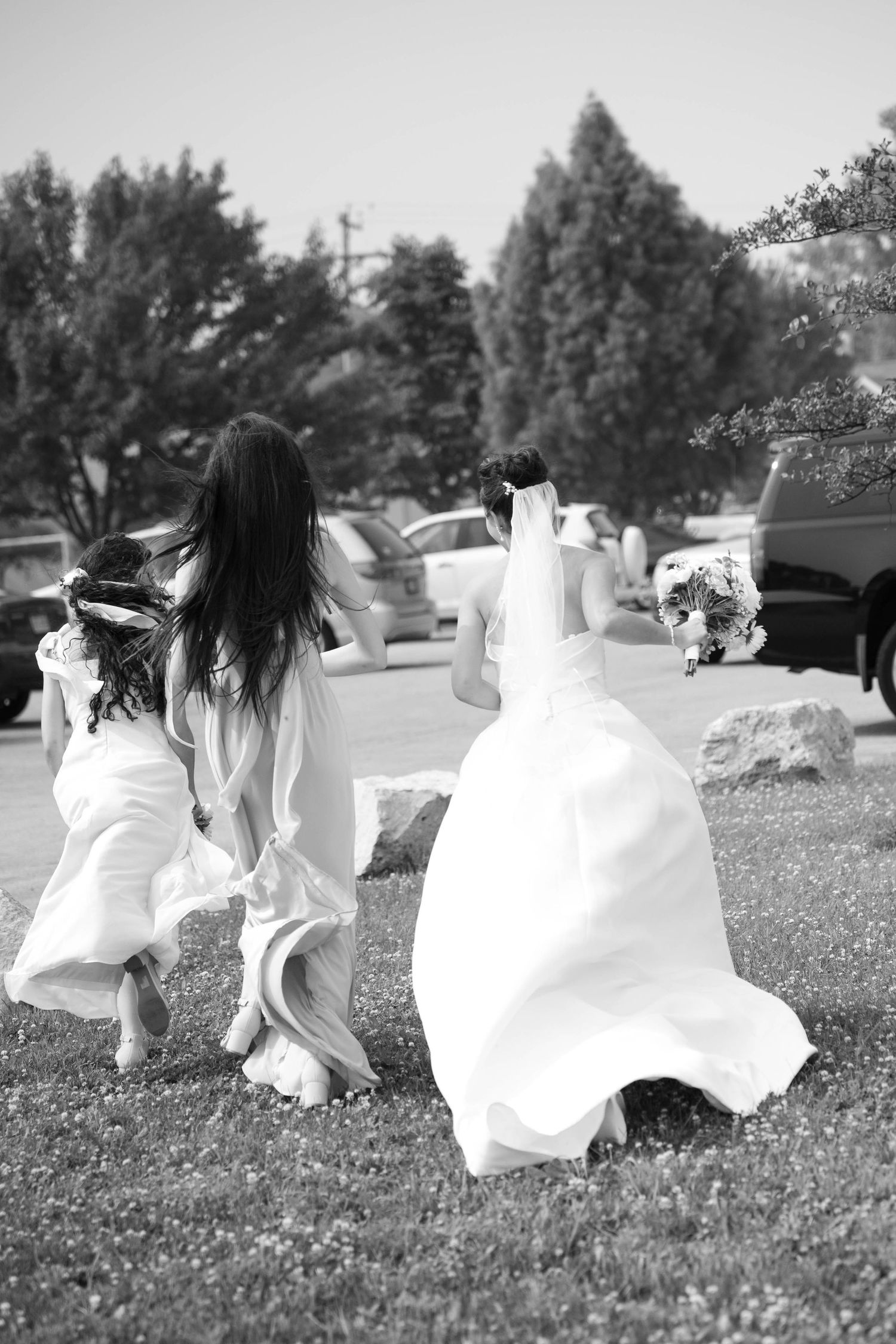 Bride and flower girl running across green lawn in white dresses on wedding day.