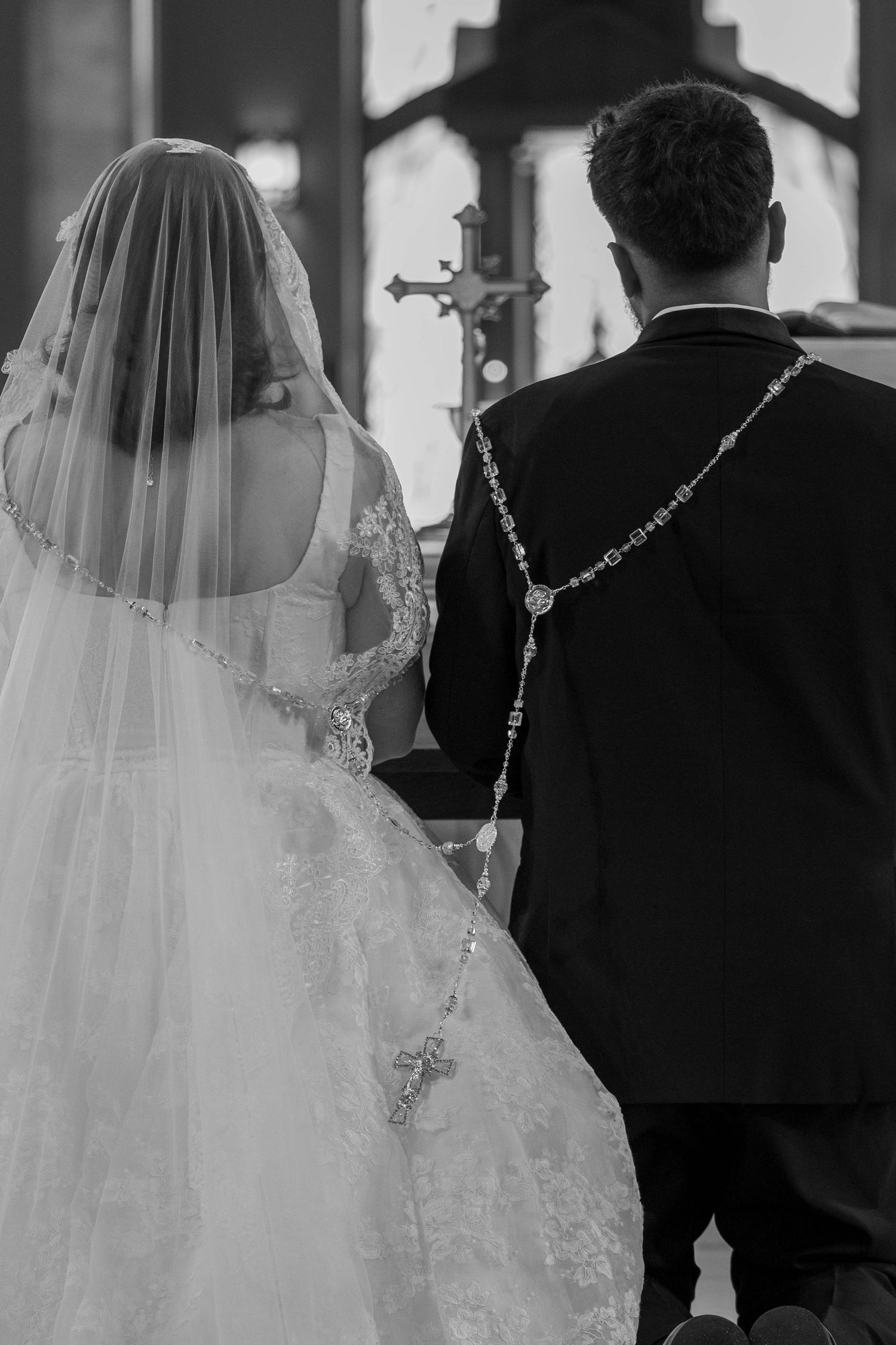 Black and white photo of a bride and groom kneeling at a church altar during their wedding ceremony.
