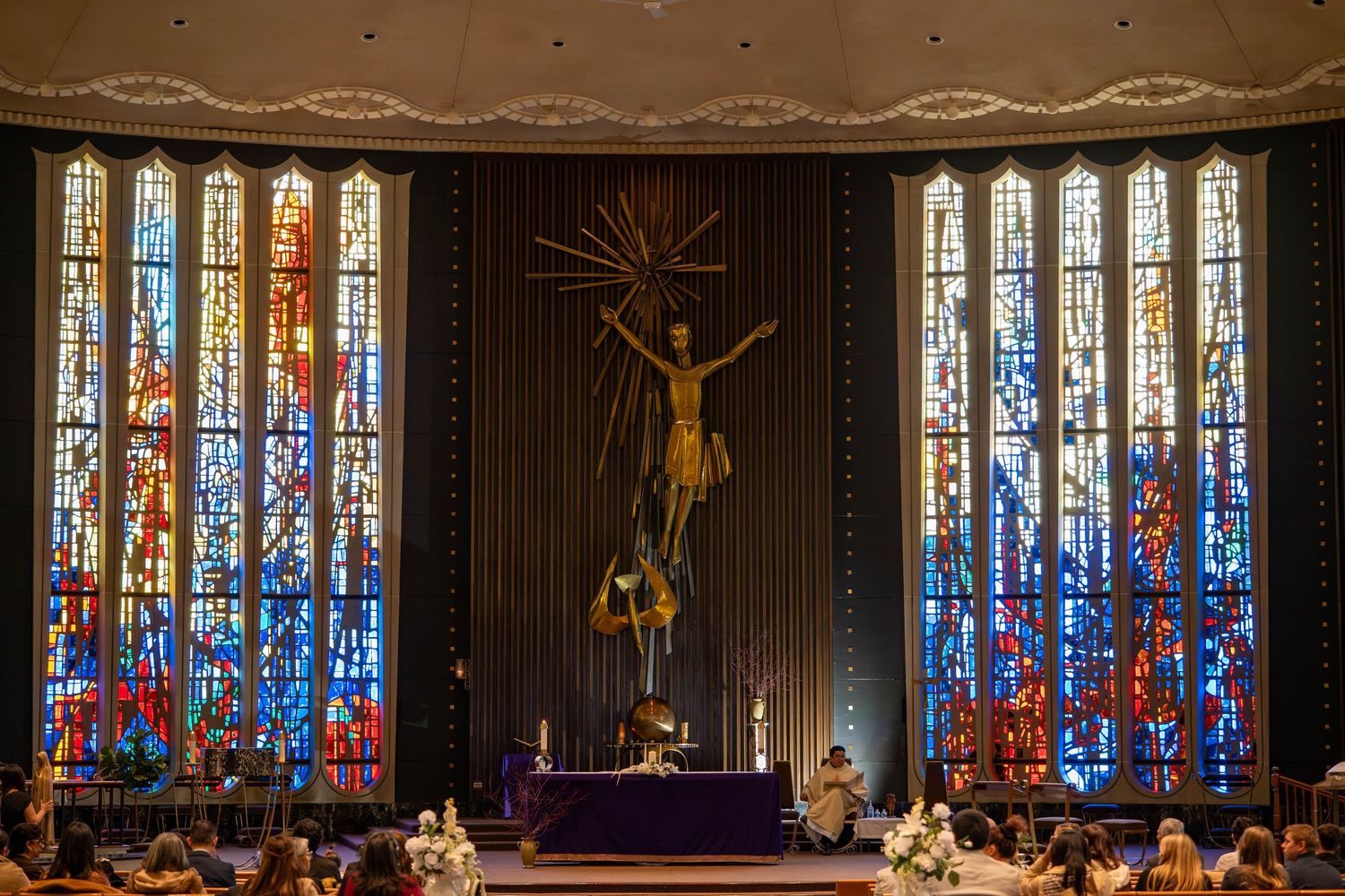 Stunning Catholic church altar with large crucifix sculpture, colorful stained glass windows, and purple Lenten decorations.