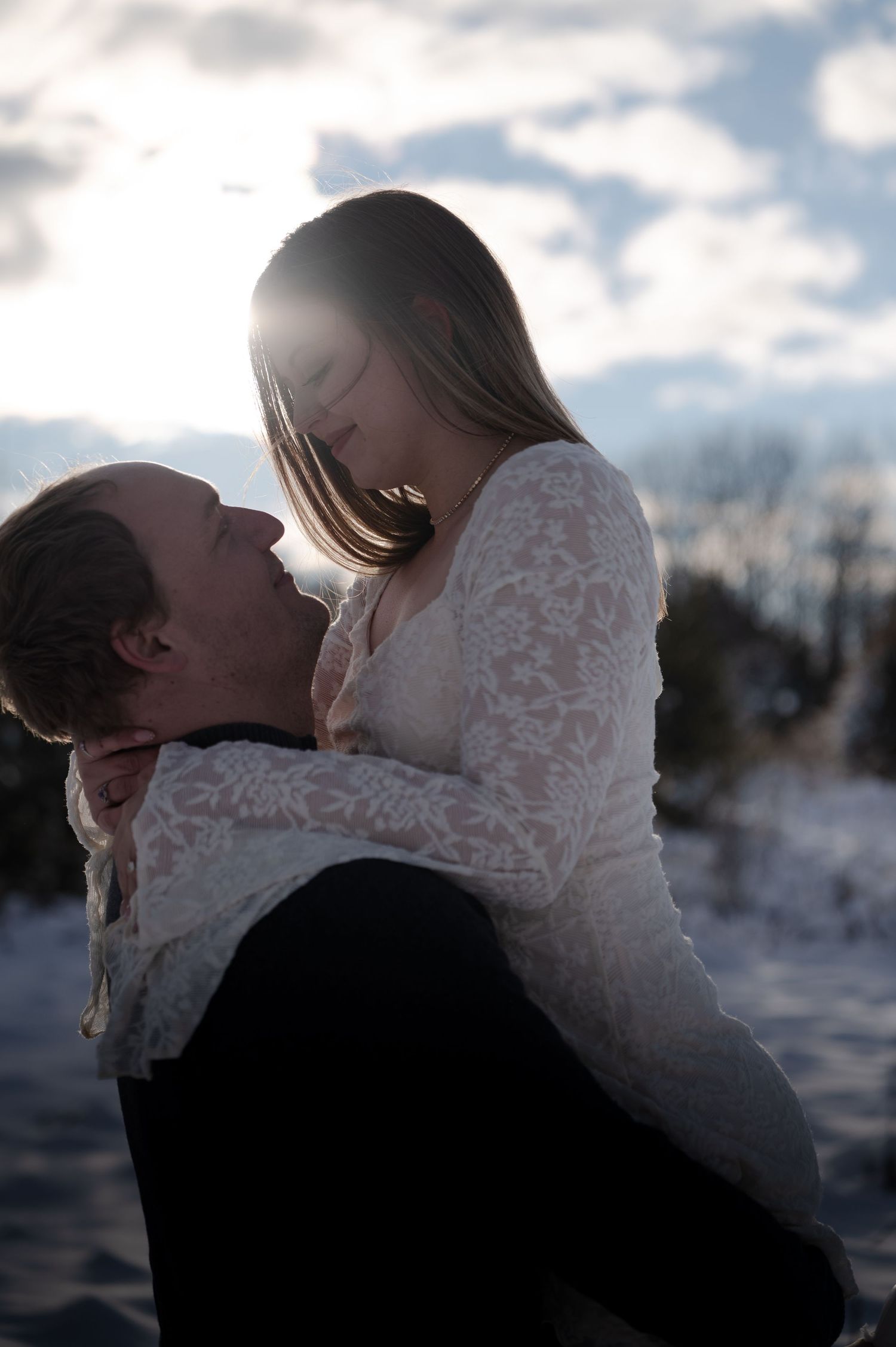 Groom lifts bride in a romantic winter embrace with sunlight glowing behind them.