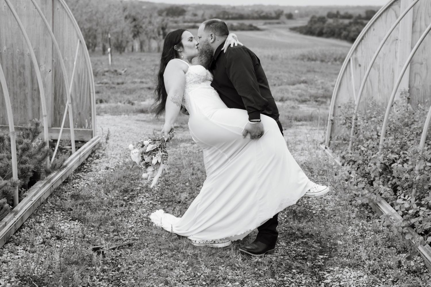 Black and white photo of a groom dipping his bride in a romantic kiss outdoors.