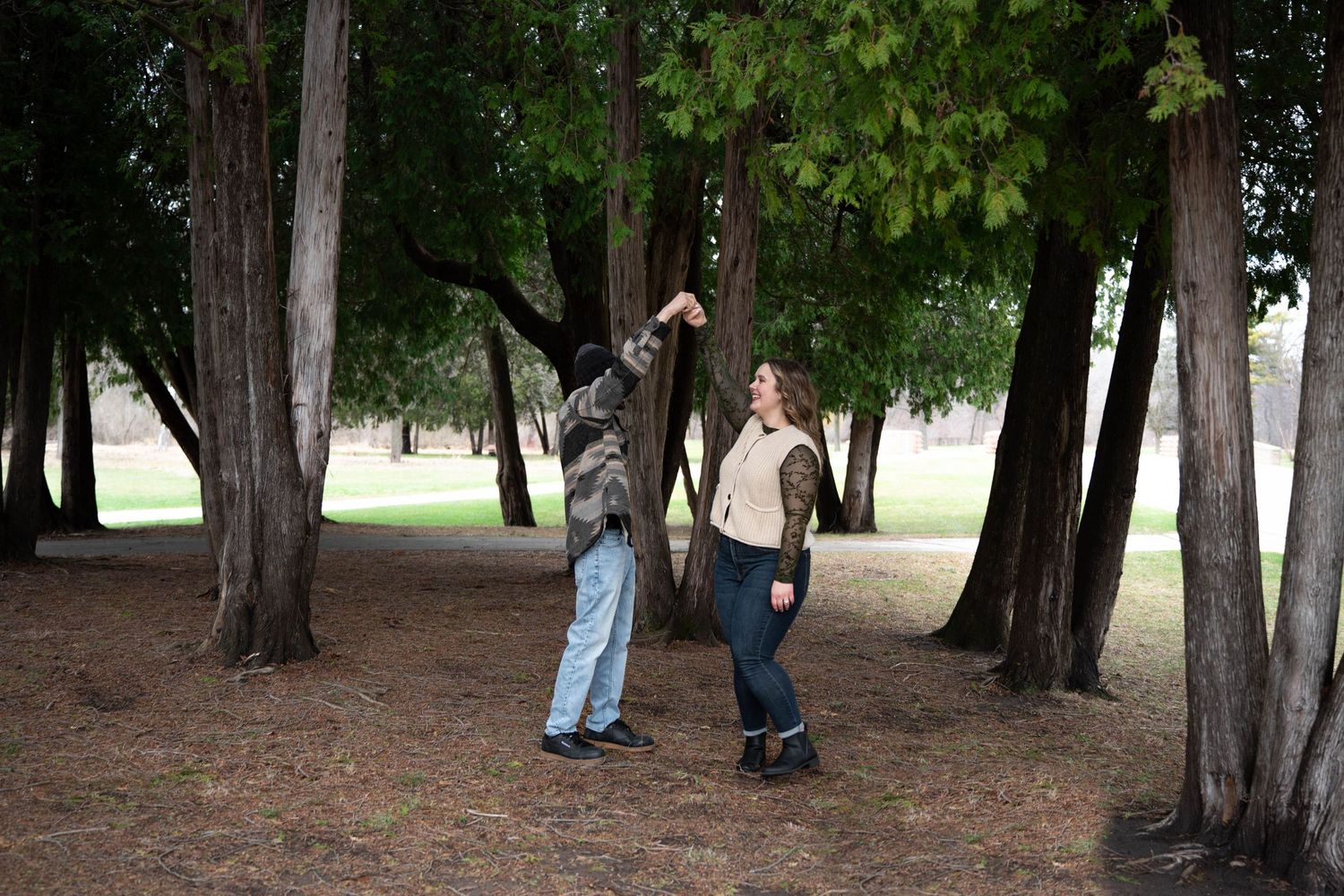Couple exploring among tall trees in a park, man pointing upward at branches.